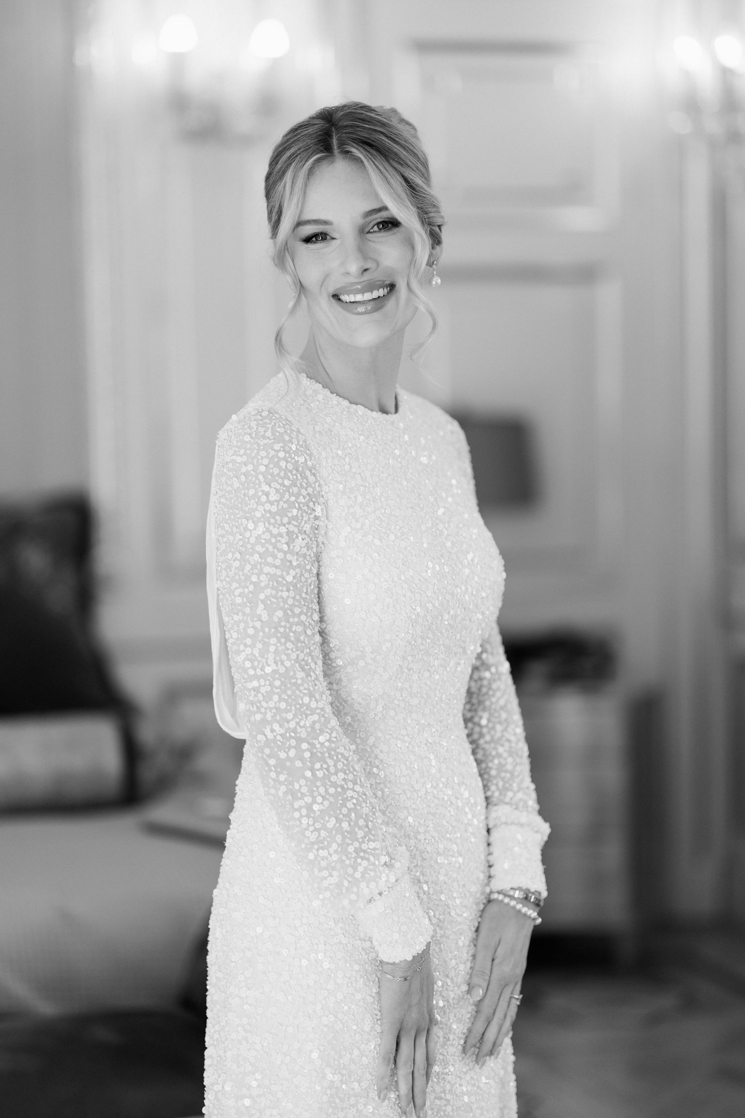Black and white portrait of a bride wearing a long-sleeved beaded wedding gown with an elegant updo hairstyle.