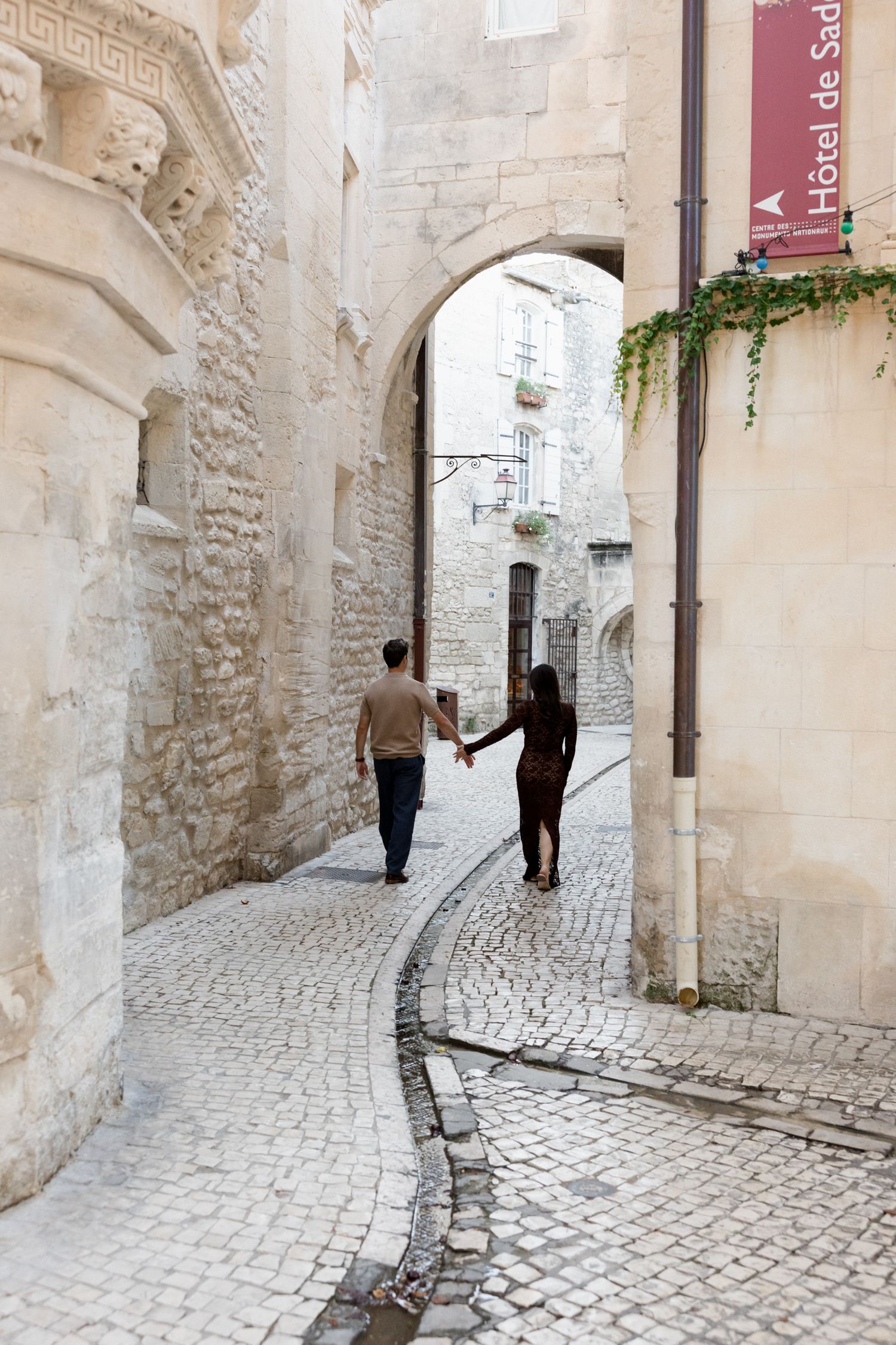 A person walks through a narrow cobblestone alley with white stone walls and arches in a historic European town. Engagement session Paris