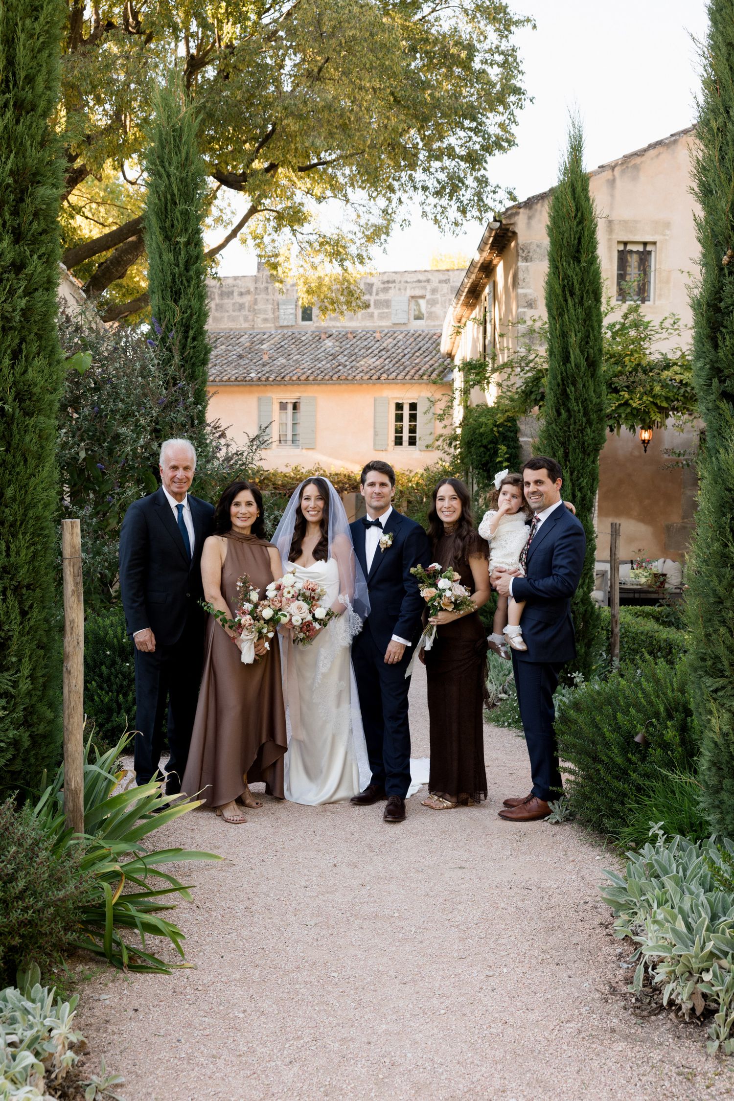 Wedding party gathered on a gravel path lined with cypress trees at a Mediterranean-style venue. wedding photographer france