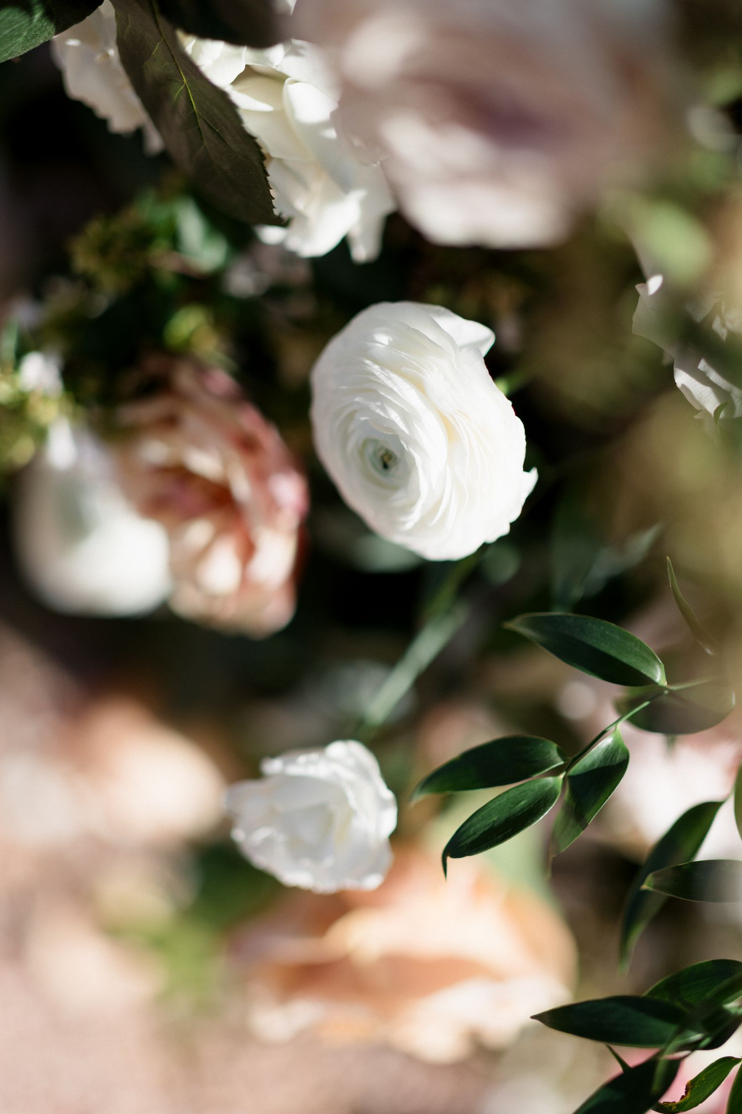 Delicate white roses and green foliage create a soft, romantic bokeh effect in a wedding floral arrangement.