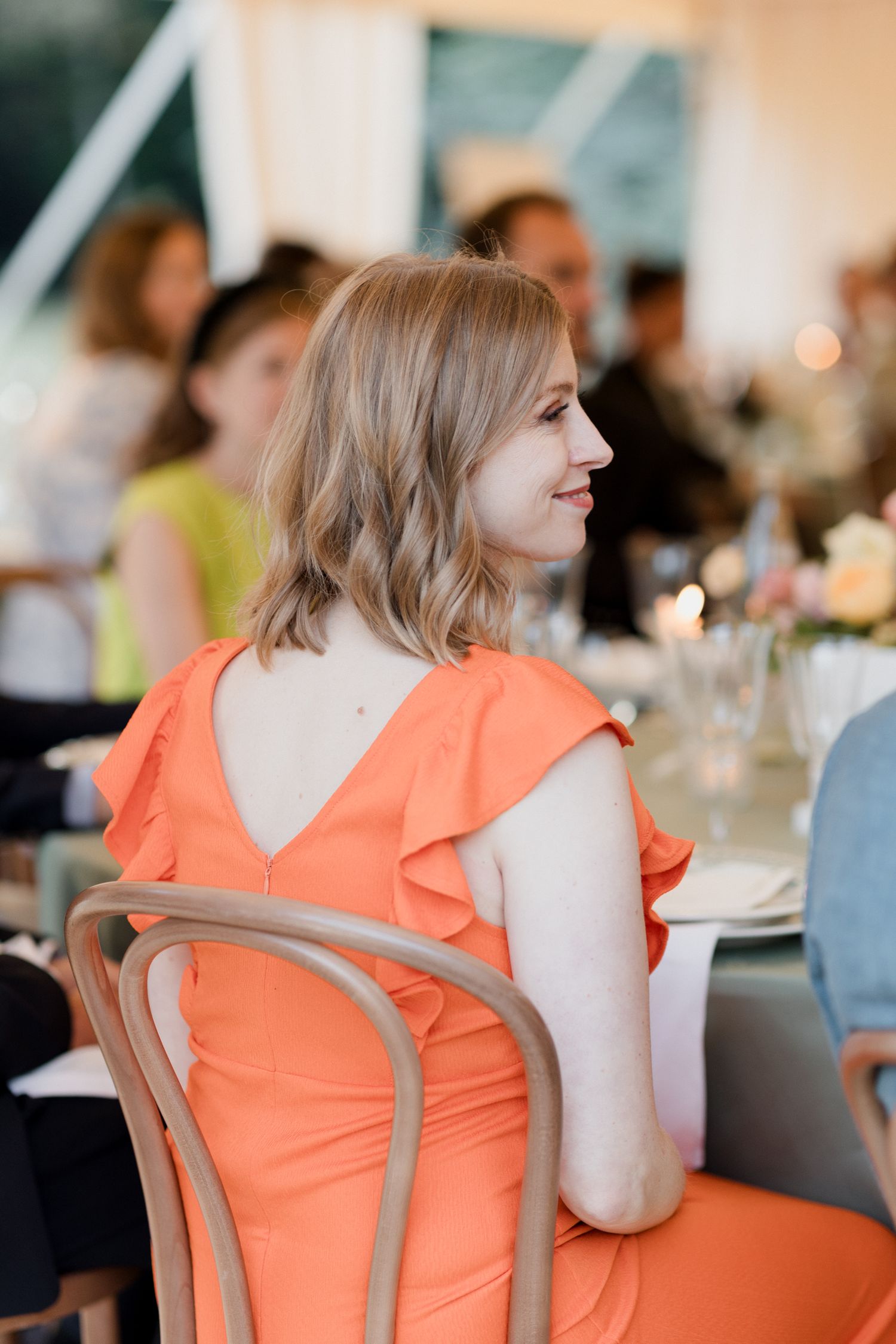 Woman in bright coral dress sitting at restaurant table shown from different side angles.