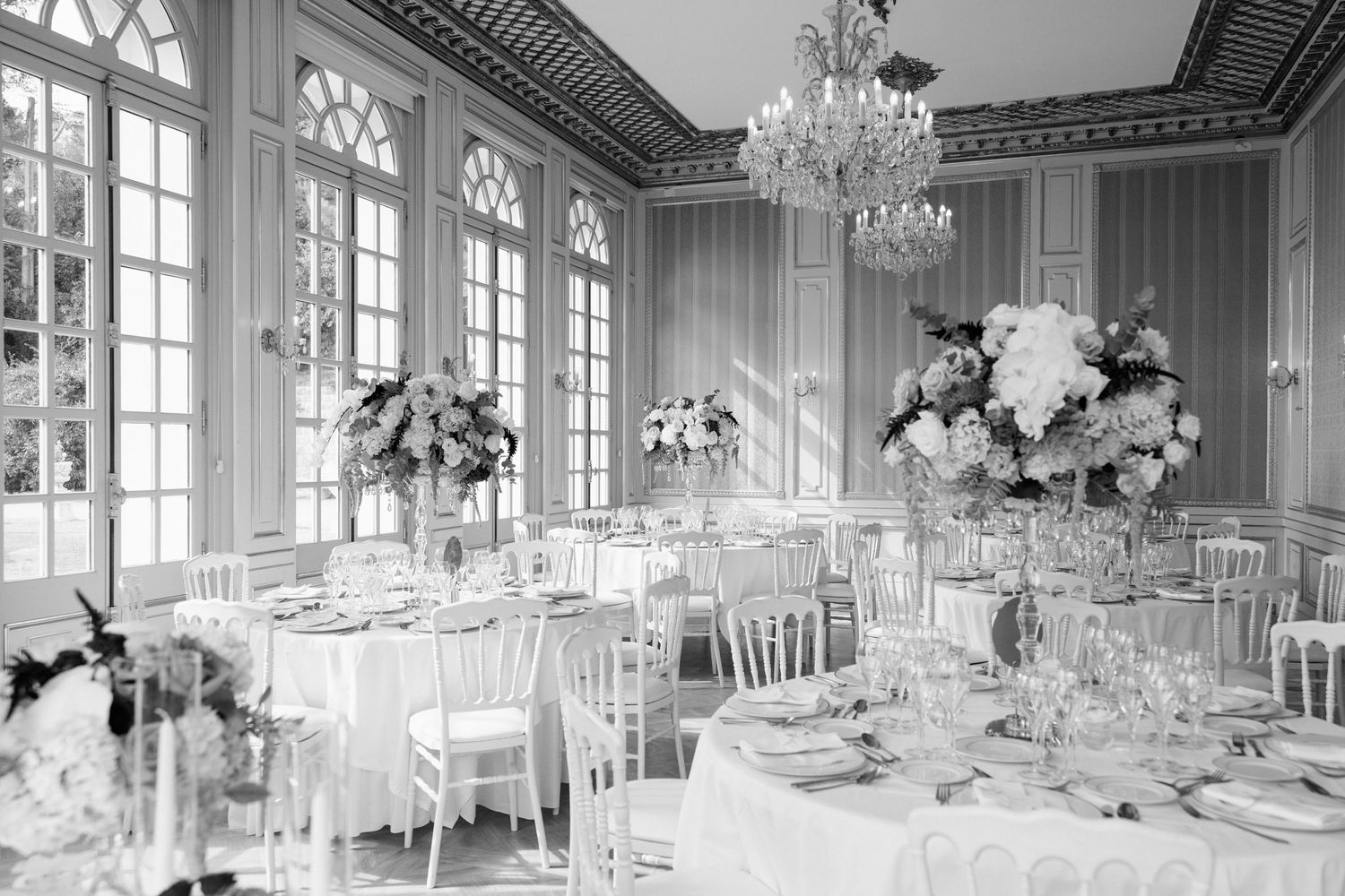 Elegant ballroom wedding reception setup with crystal chandeliers, round tables, and white floral centerpieces.