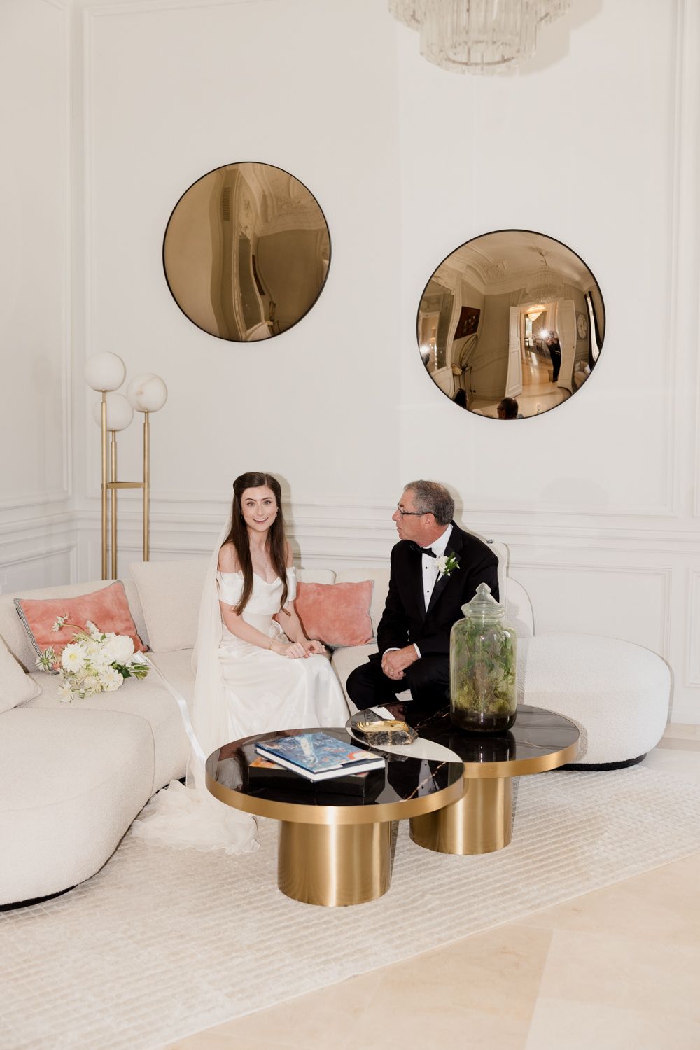 Two people sit at a sleek modern table with gold accents in a minimalist white interior design space.