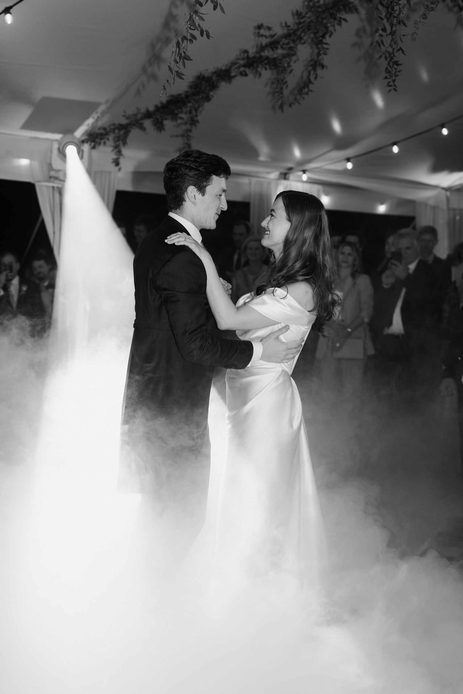 Newlyweds share their first dance surrounded by fog effects and romantic lighting at wedding reception.