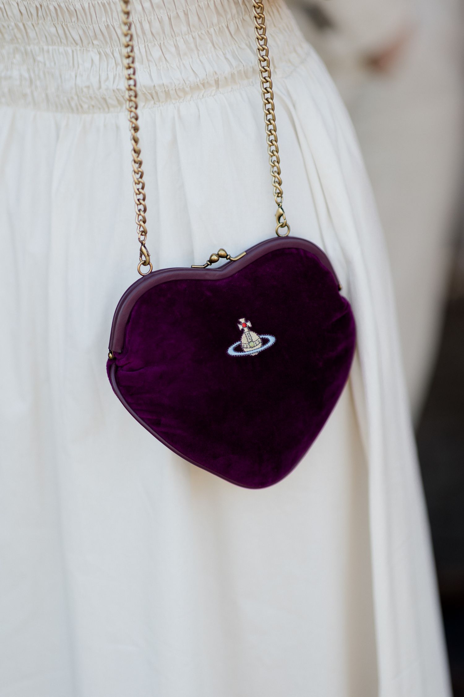 Purple velvet heart-shaped purse with gold chain strap against white fabric background. Loire valley wedding photographer