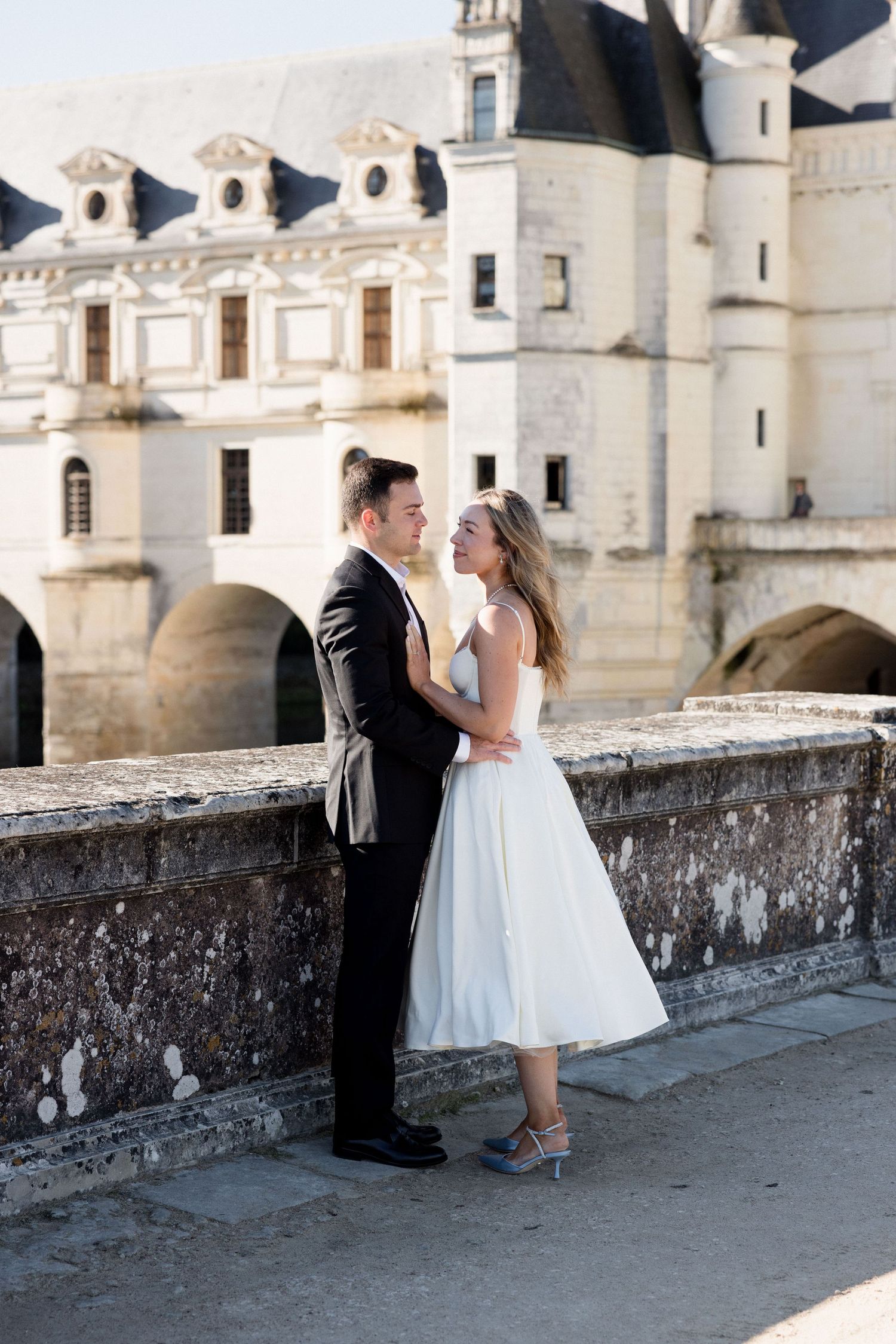 Bride and groom embracing romantically in front of stunning white French Renaissance chateau.