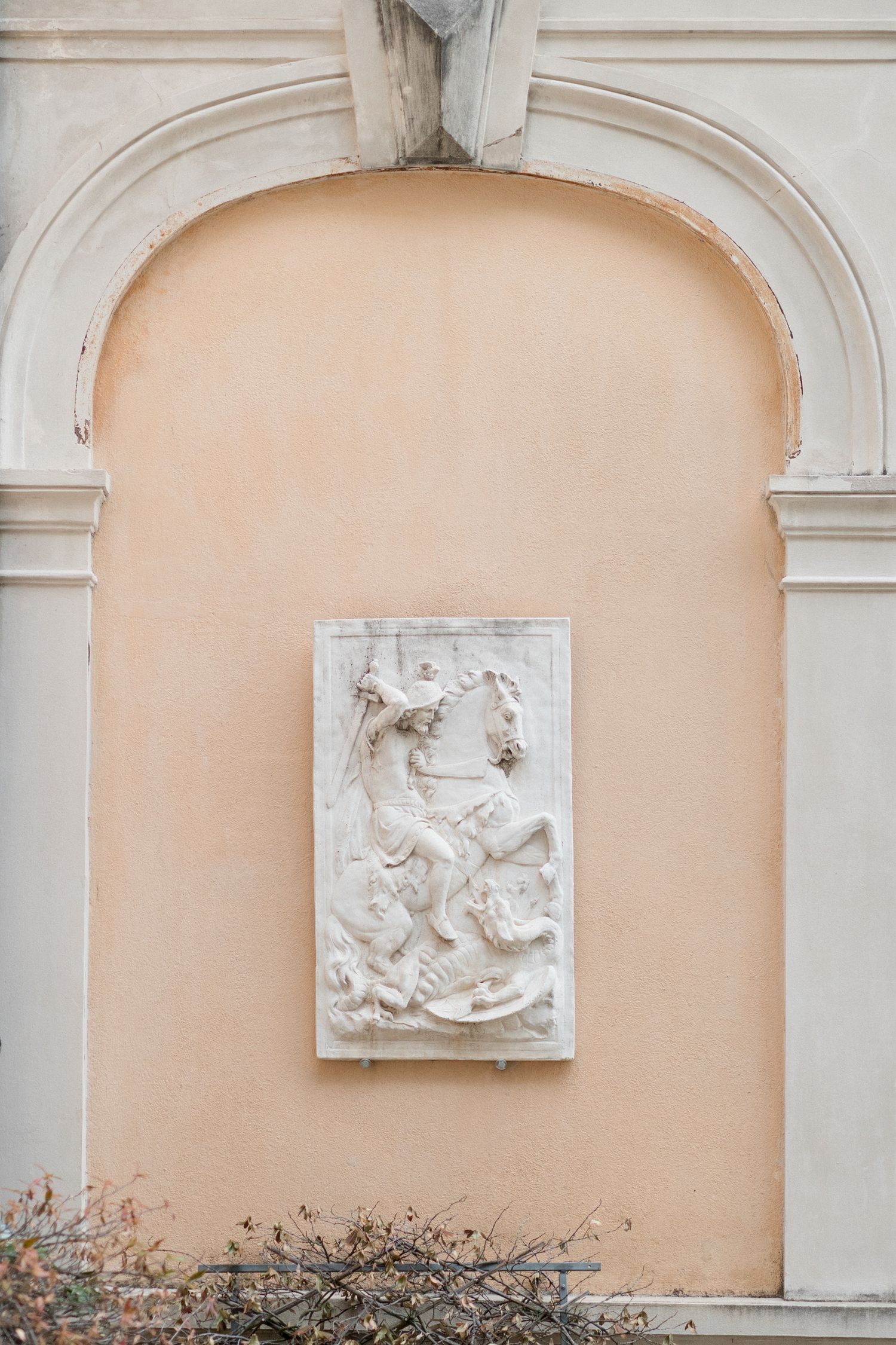Sequence of architectural wall niches with ornate white relief sculptures mounted on a peach-colored background.