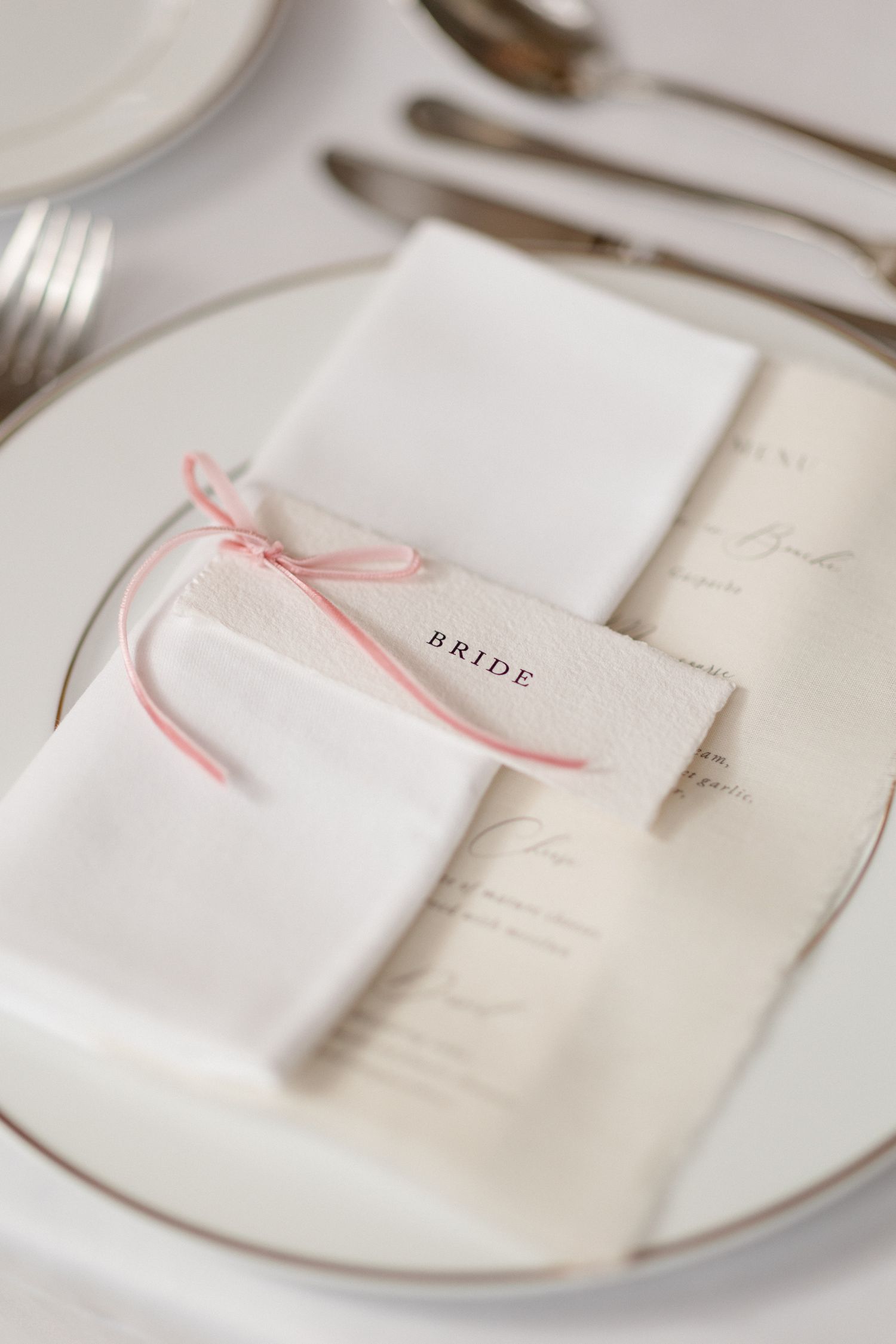 White plates with delicate pink ribbon details arranged in a minimalist table setting. destination wedding france Mariage Grasse