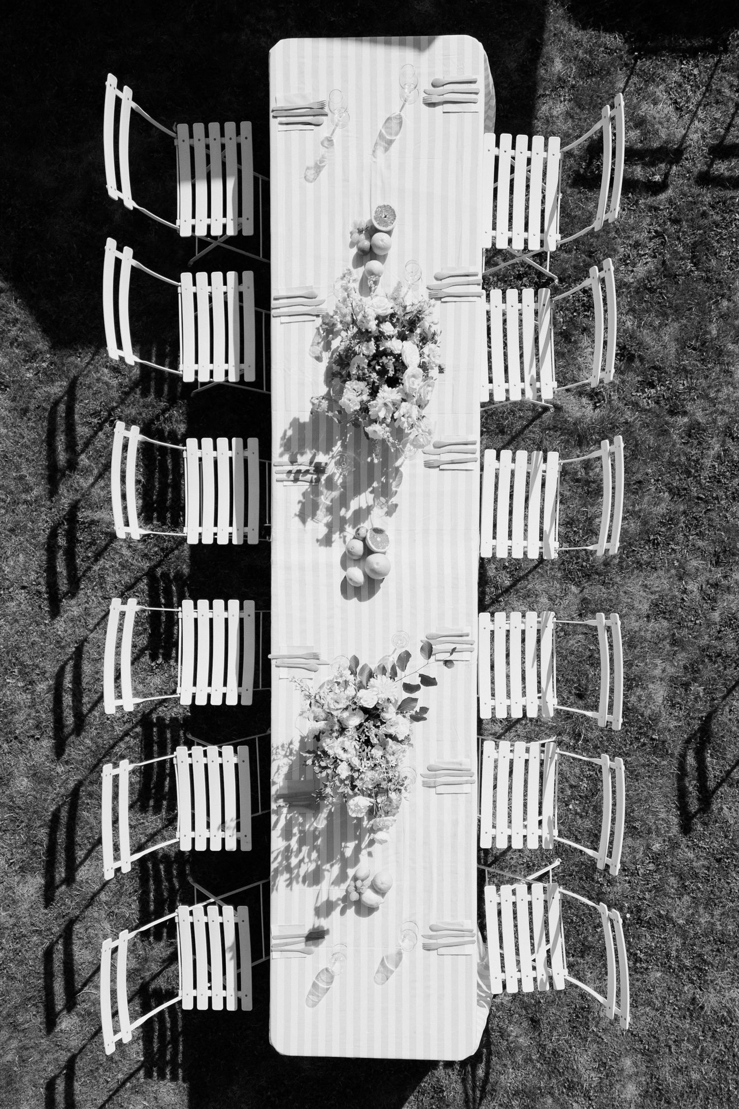 Aerial black and white view of a long white table with chairs set up outdoors on grass for an event. Pool party loire valley