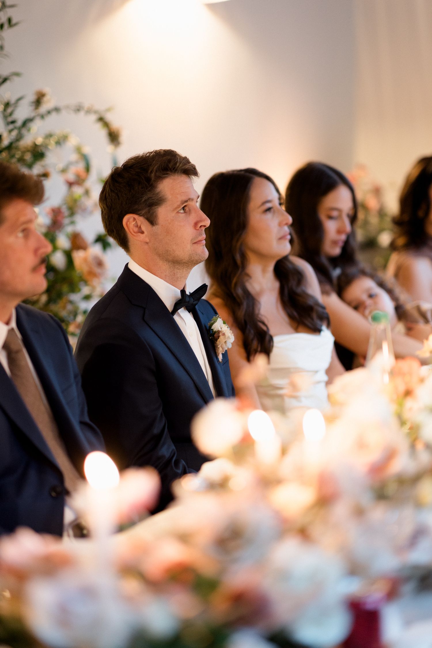 Wedding guests seated at an elegant reception dinner table with soft lighting and floral centerpieces. wedding photographer france