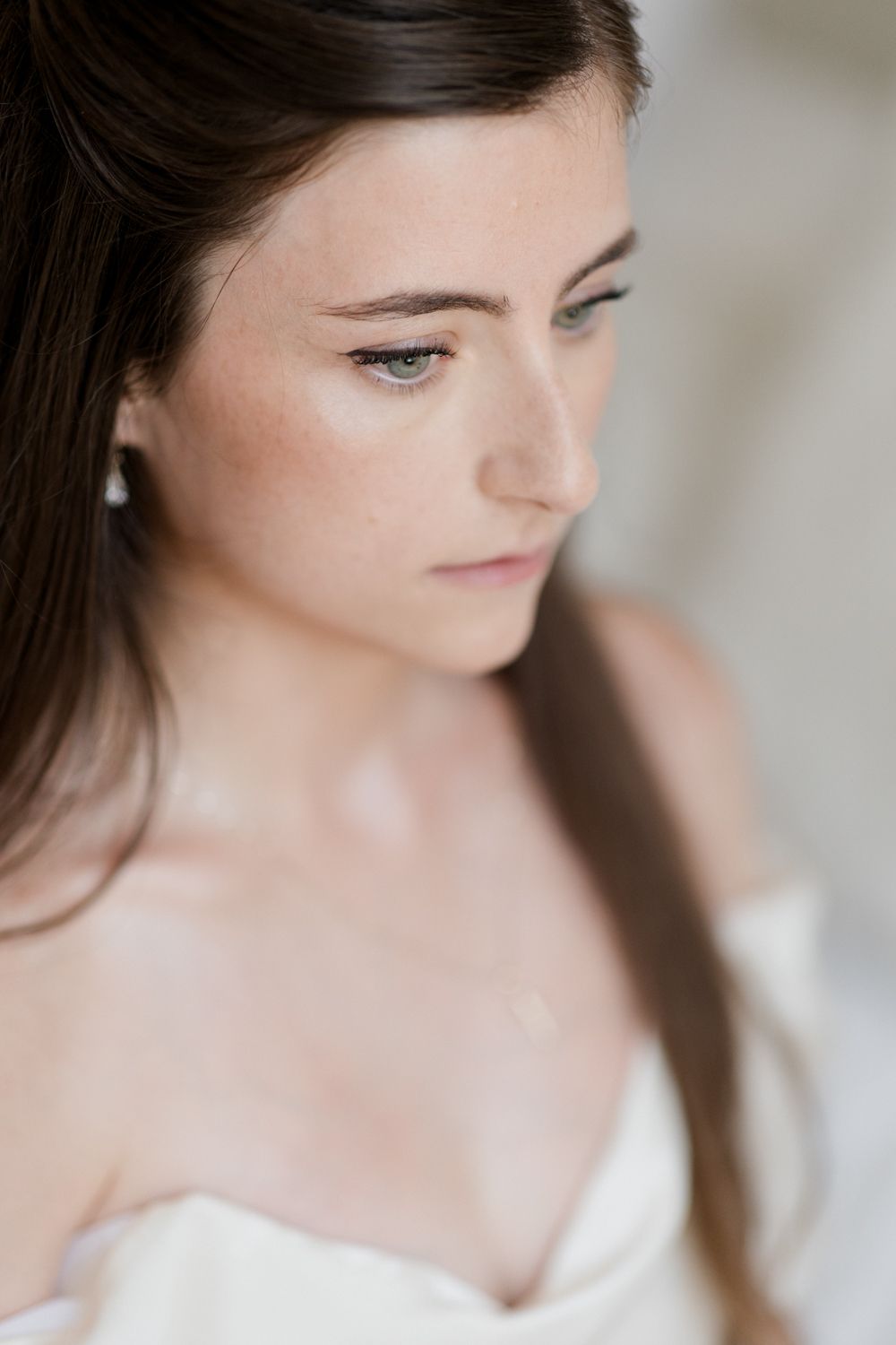 A soft-focused portrait shows a contemplative downward gaze and white off-shoulder attire in natural lighting. Photographe mariage Tours
