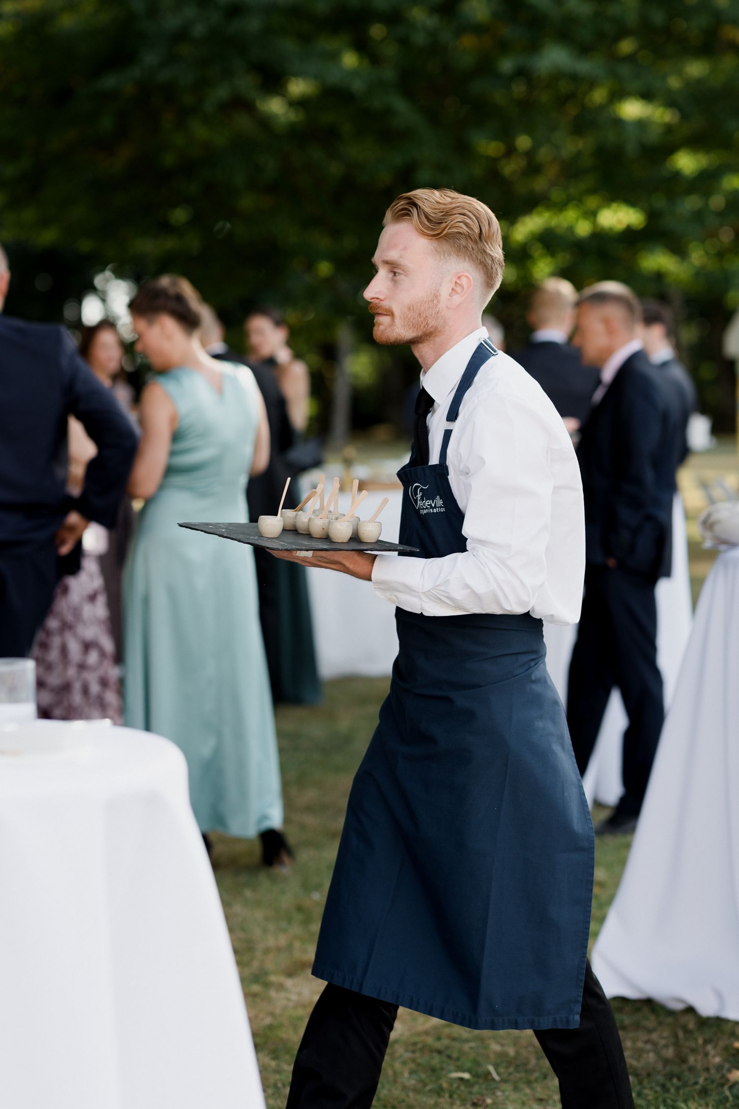 Wedding guests mingle and socialize during an outdoor reception in a garden setting.
