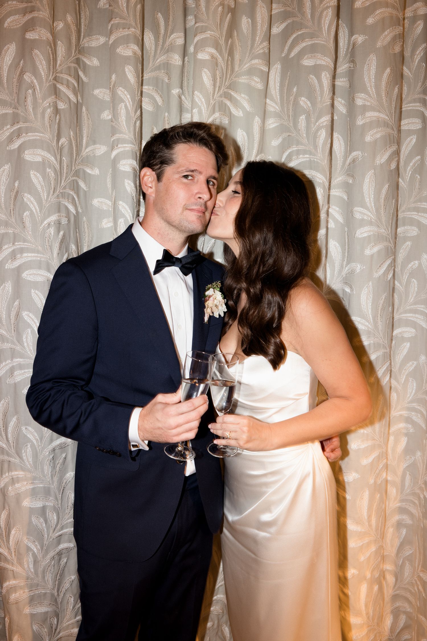 A couple in formal attire share a romantic dance together at an event with a white curtain backdrop. wedding photographer france editorial