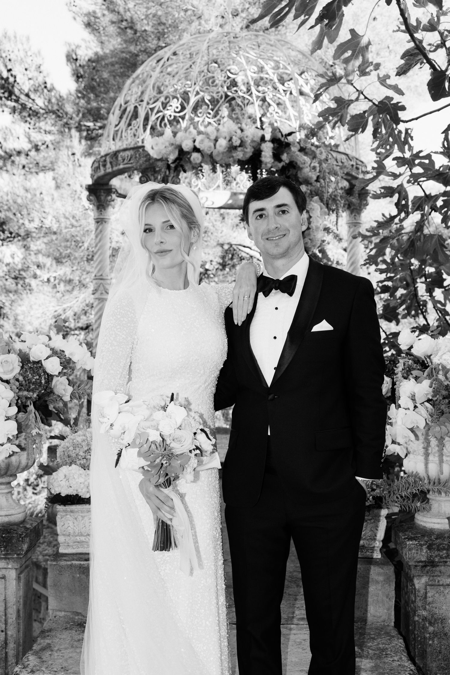 A series of black and white wedding photos showing a couple posing together with floral decorations in an outdoor setting.