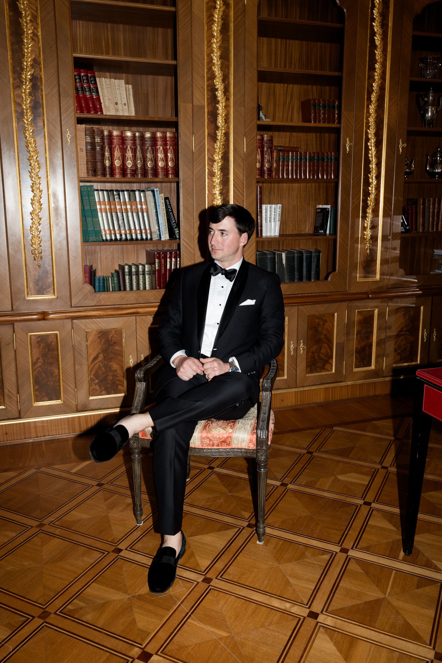 A figure in a tuxedo sits in an elegant library with wood paneling and ornate gold trim details. Mariage Chateau saint georges Grasse France