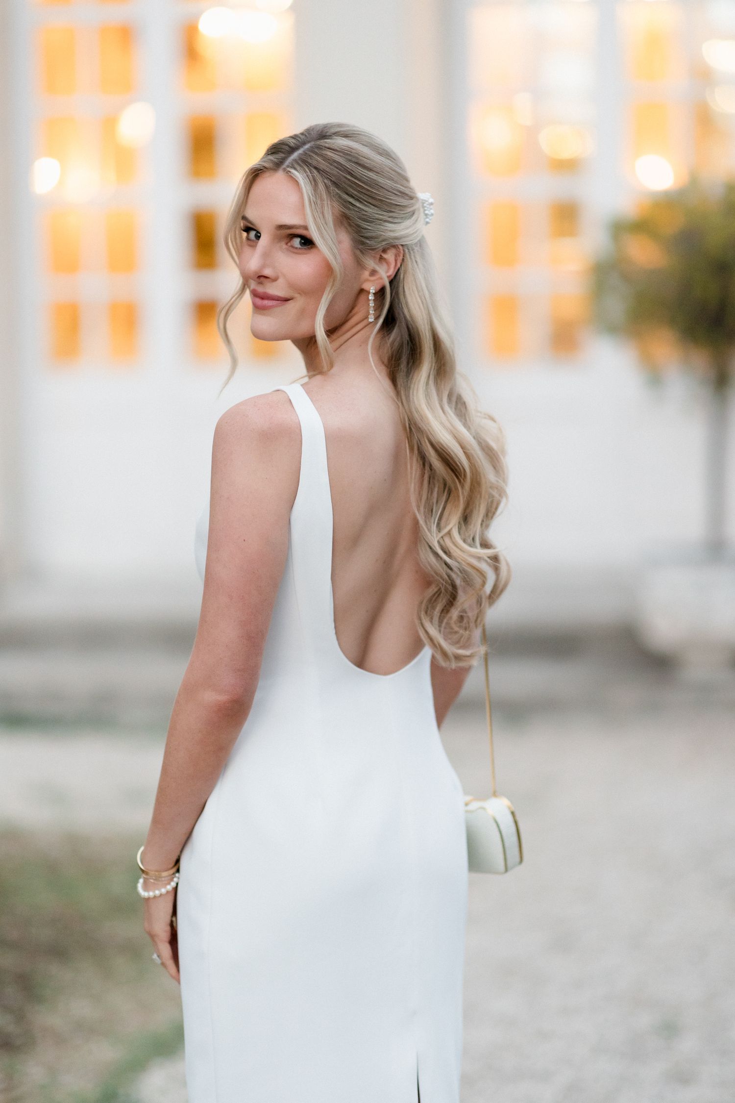 Woman in white sleeveless dress poses outdoors with blonde hair and natural lighting at sunset. destination wedding france