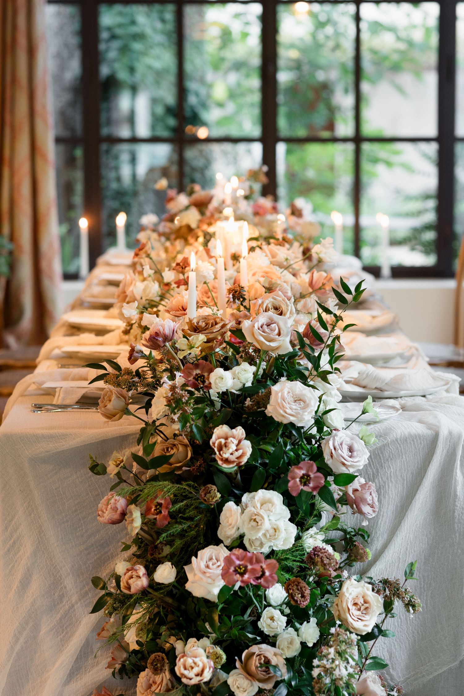 Elegant wedding reception tables with white linens and blush pink rose centerpieces in a sunlit venue with large windows. wedding photograph