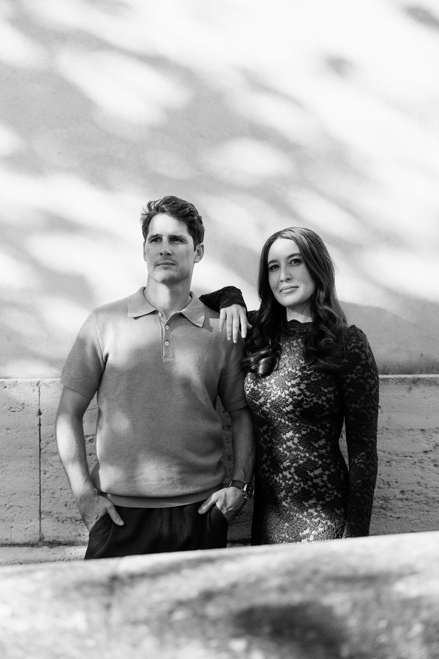 A couple poses together on a beach in black and white, with cloudy skies in the background.