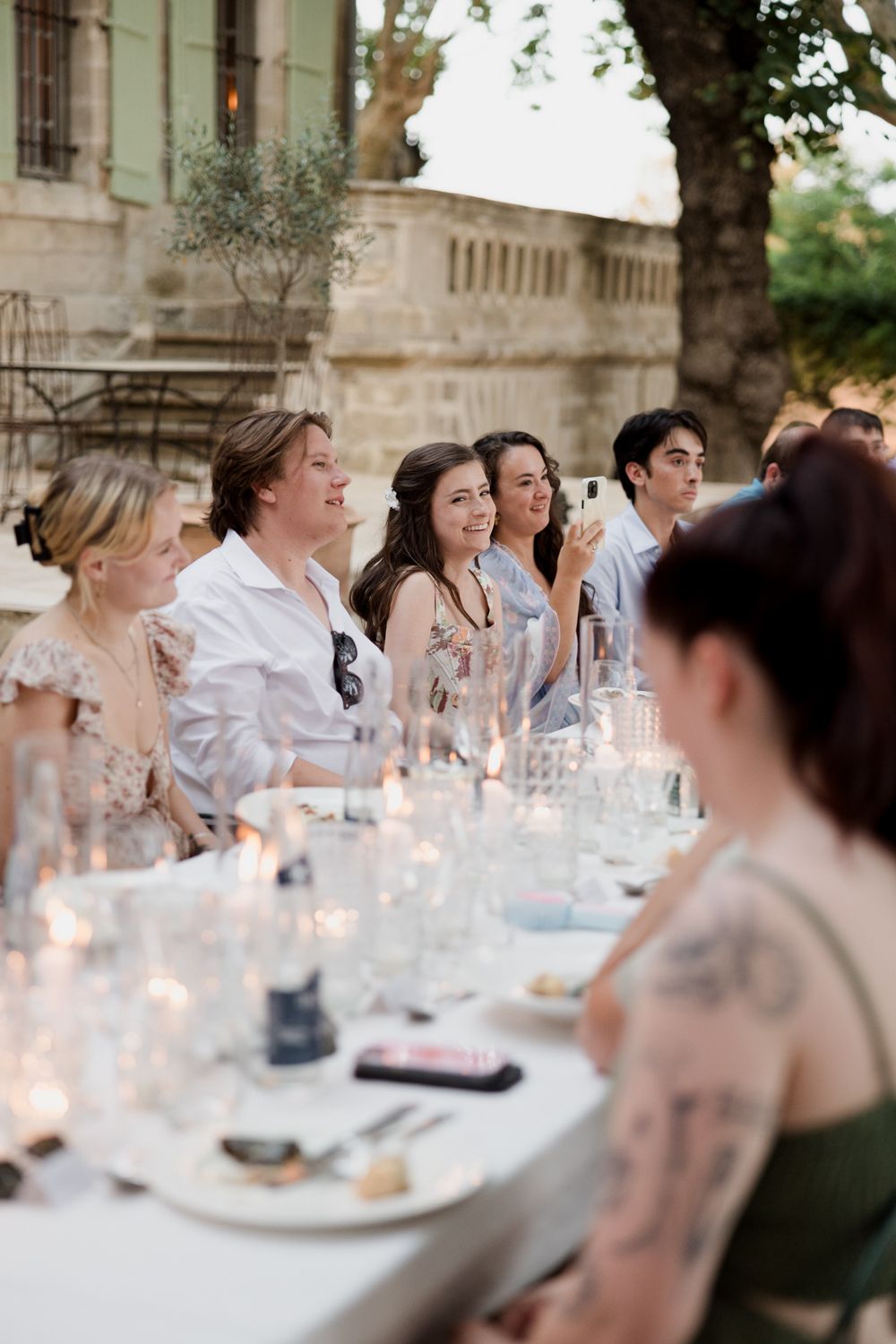 Guests enjoy an elegant outdoor dinner party at long tables adorned with glowing candles at dusk.