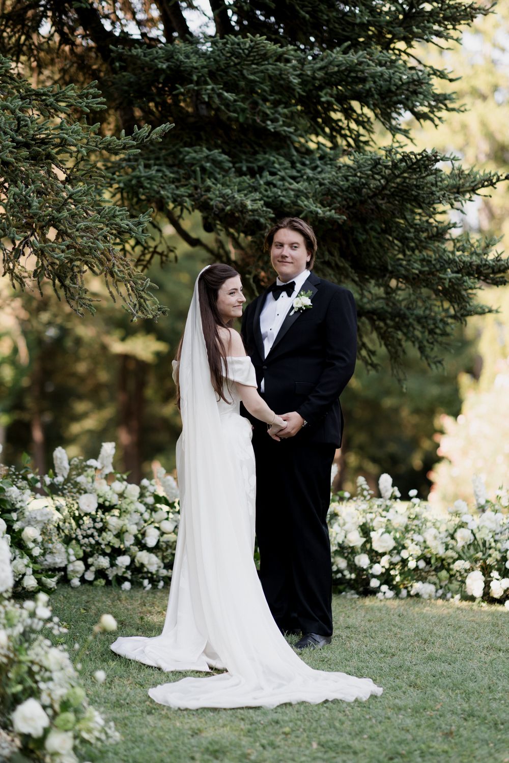 Romantic outdoor wedding portrait series with couple posing in garden setting with white floral backdrop. Château des 3 Fontaines wedding