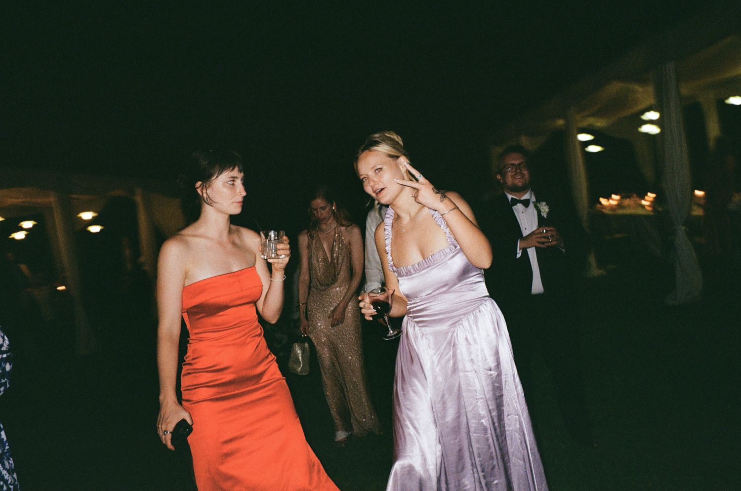 People in formal evening attire dance and mingle at a dimly lit indoor social gathering.