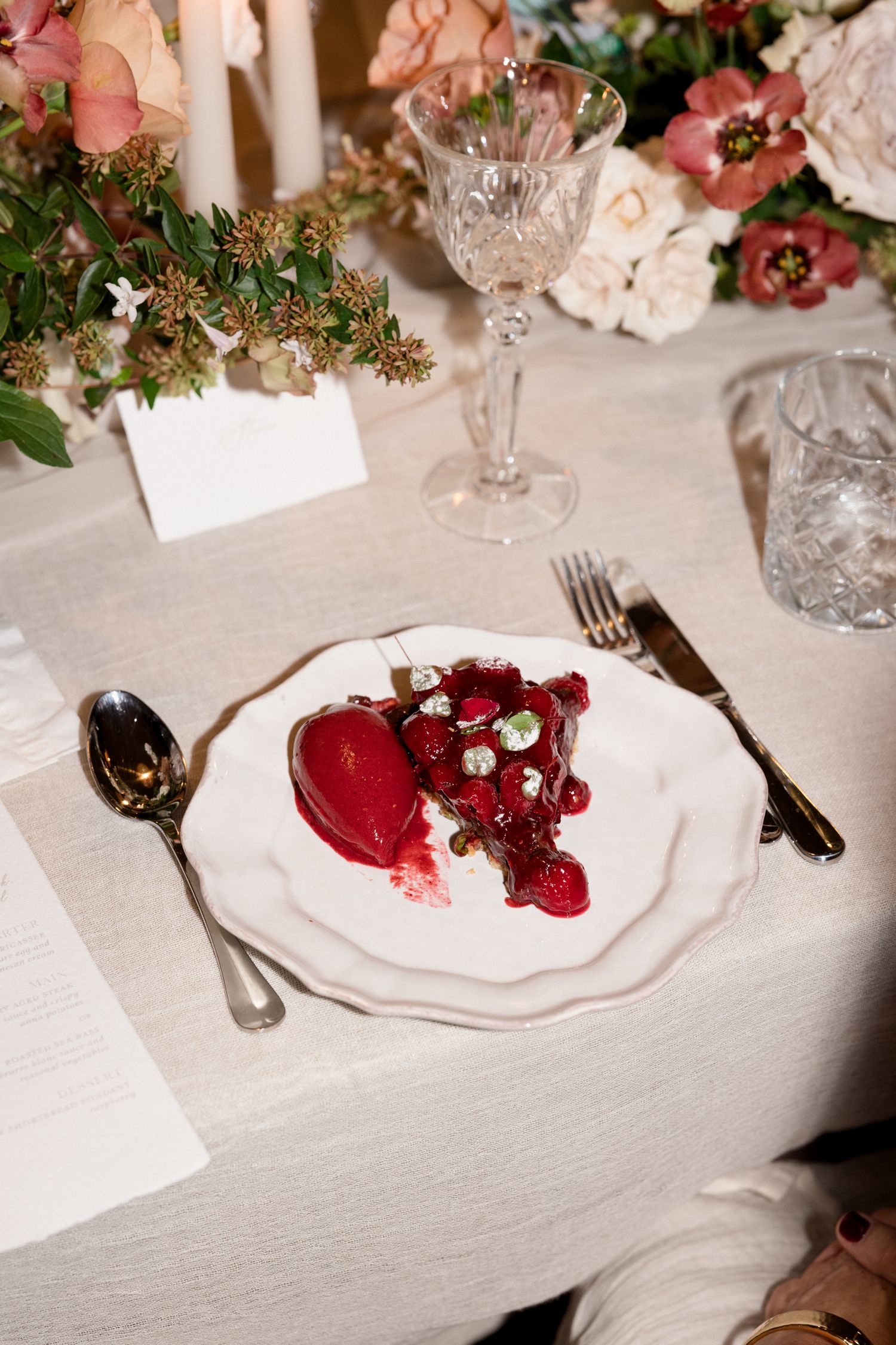 Elegant table setting with white plates and red berry desserts arranged on a light linen tablecloth with floral decorations. wedding photo