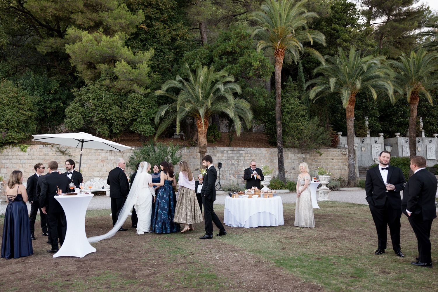 Wedding ceremony guests gather outdoors under palm trees at a scenic venue during a daytime celebration.