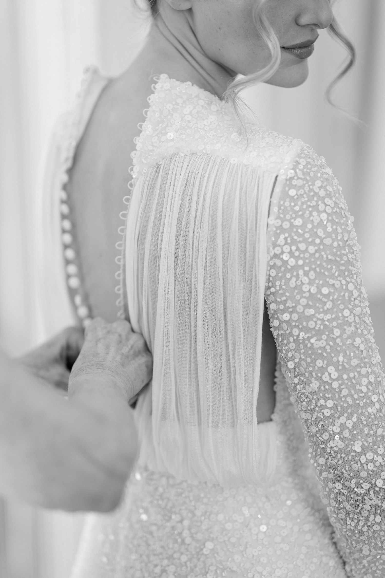 Close-up details of a wedding dress with delicate beading and flowing fabric in soft white tones.