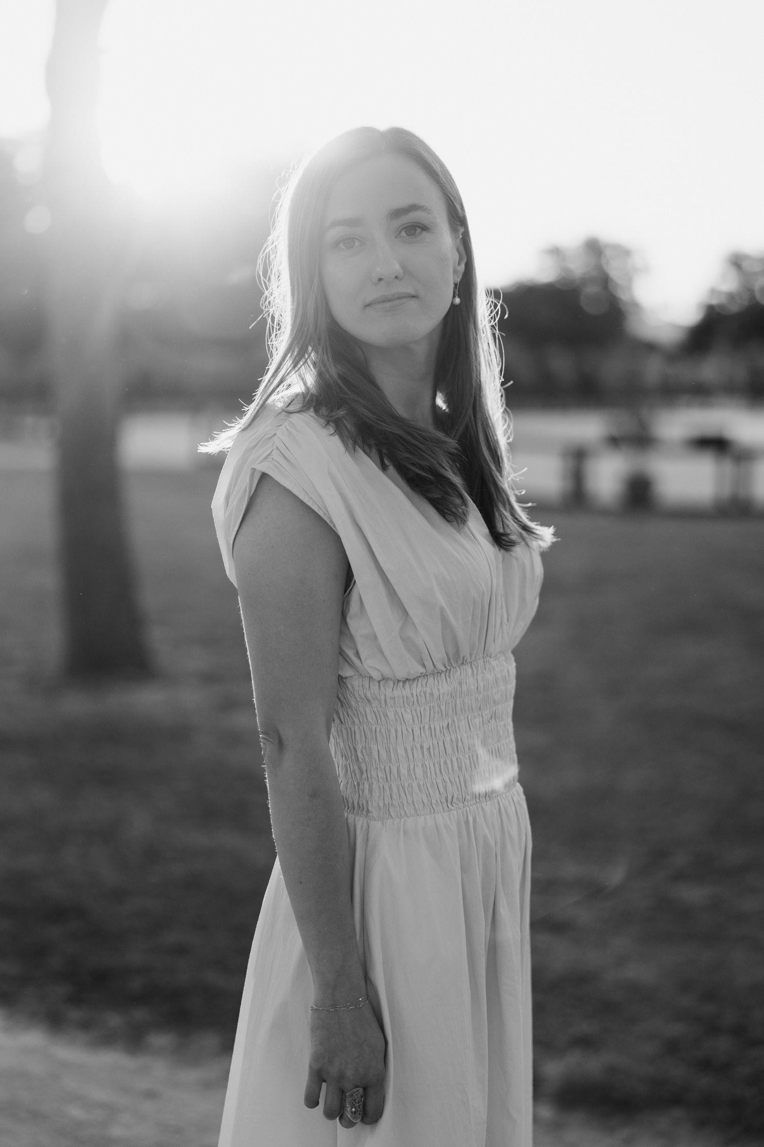 A dreamy black and white photo series shows someone in a white summer dress standing in a sunlit field.