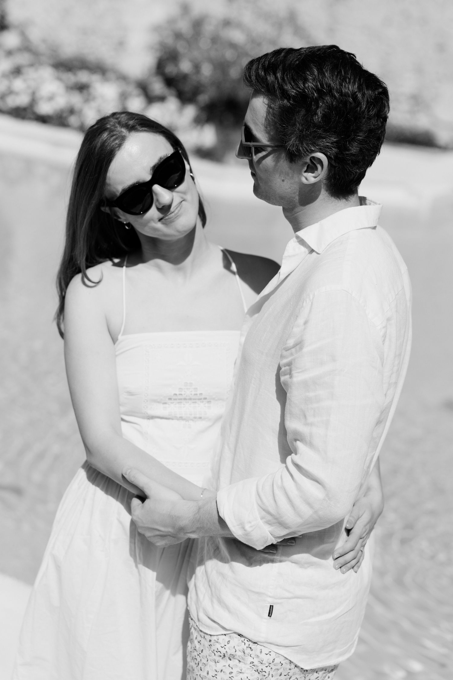 A romantic black and white photo series showing a couple embracing on the beach in white attire.