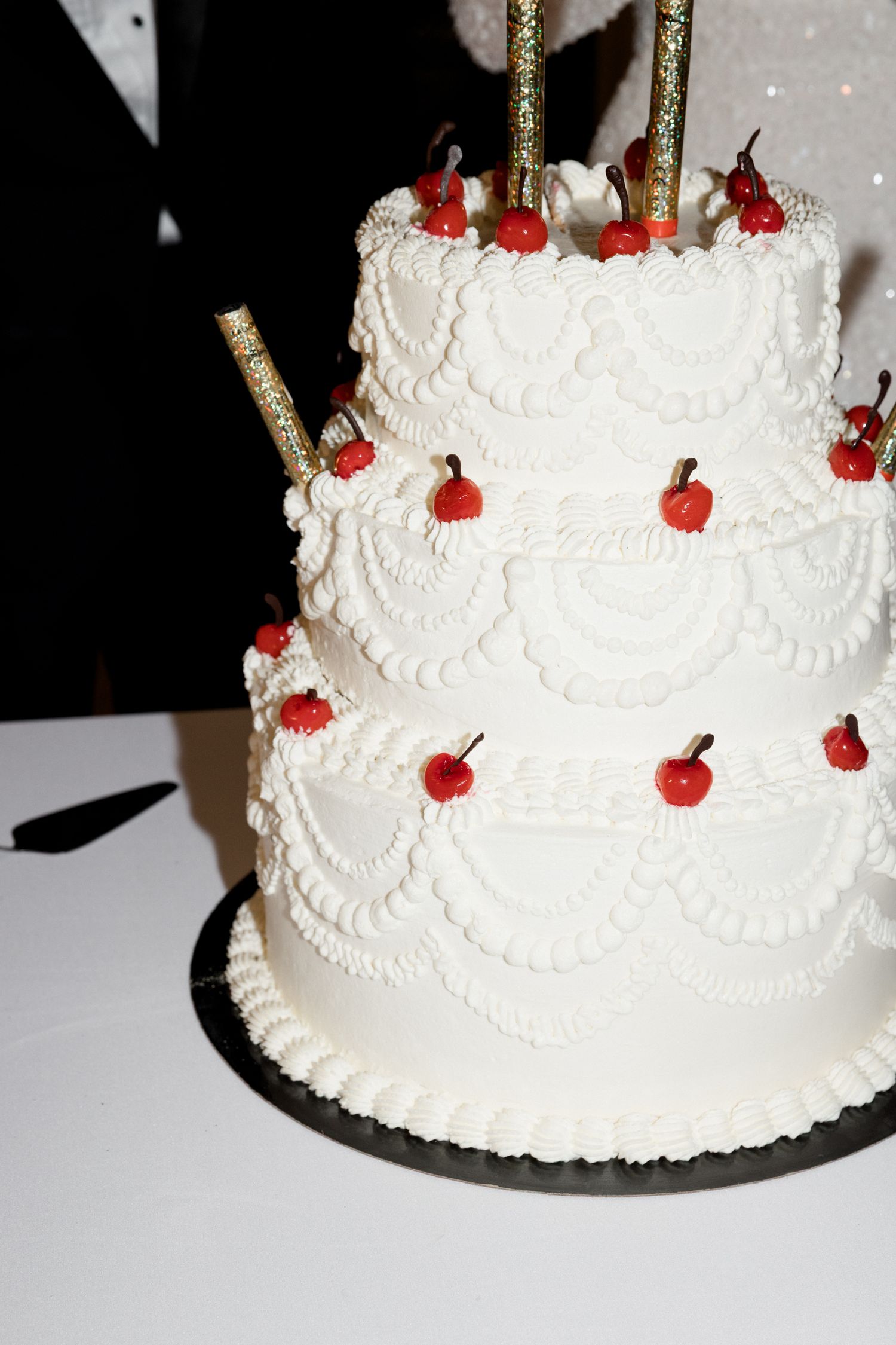 A white tiered wedding cake with delicate piped details and red cherry decorations on top viewed from different angles. french riviera wed