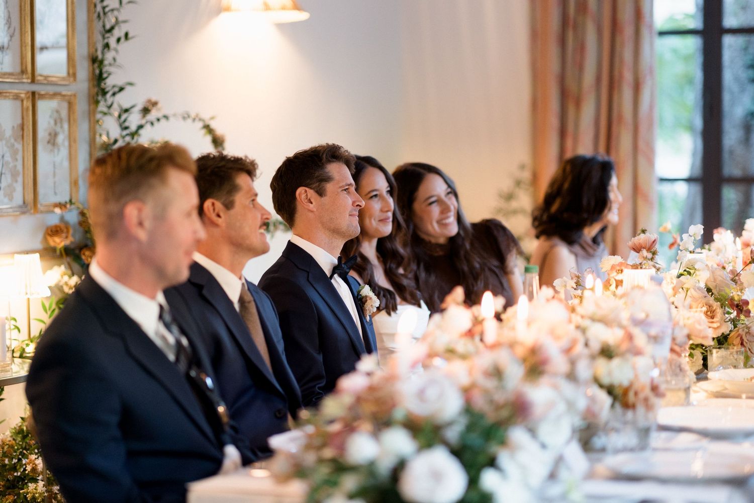 Elegant wedding reception table setting with pink floral centerpieces and glowing candles in a bright banquet hall.