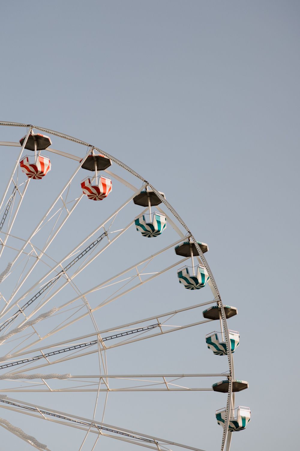 Geometric pattern of a rotating carnival ride arm with suspended seats against a pale blue sky. Seance couple Tours