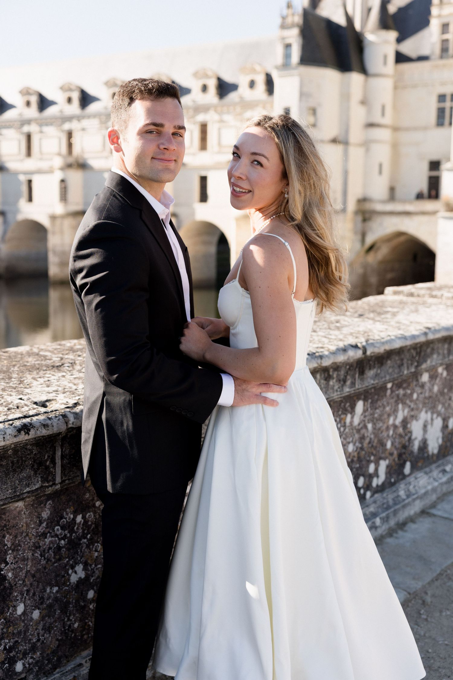 Newlyweds embracing on a bridge with a stunning French chateau in the background.