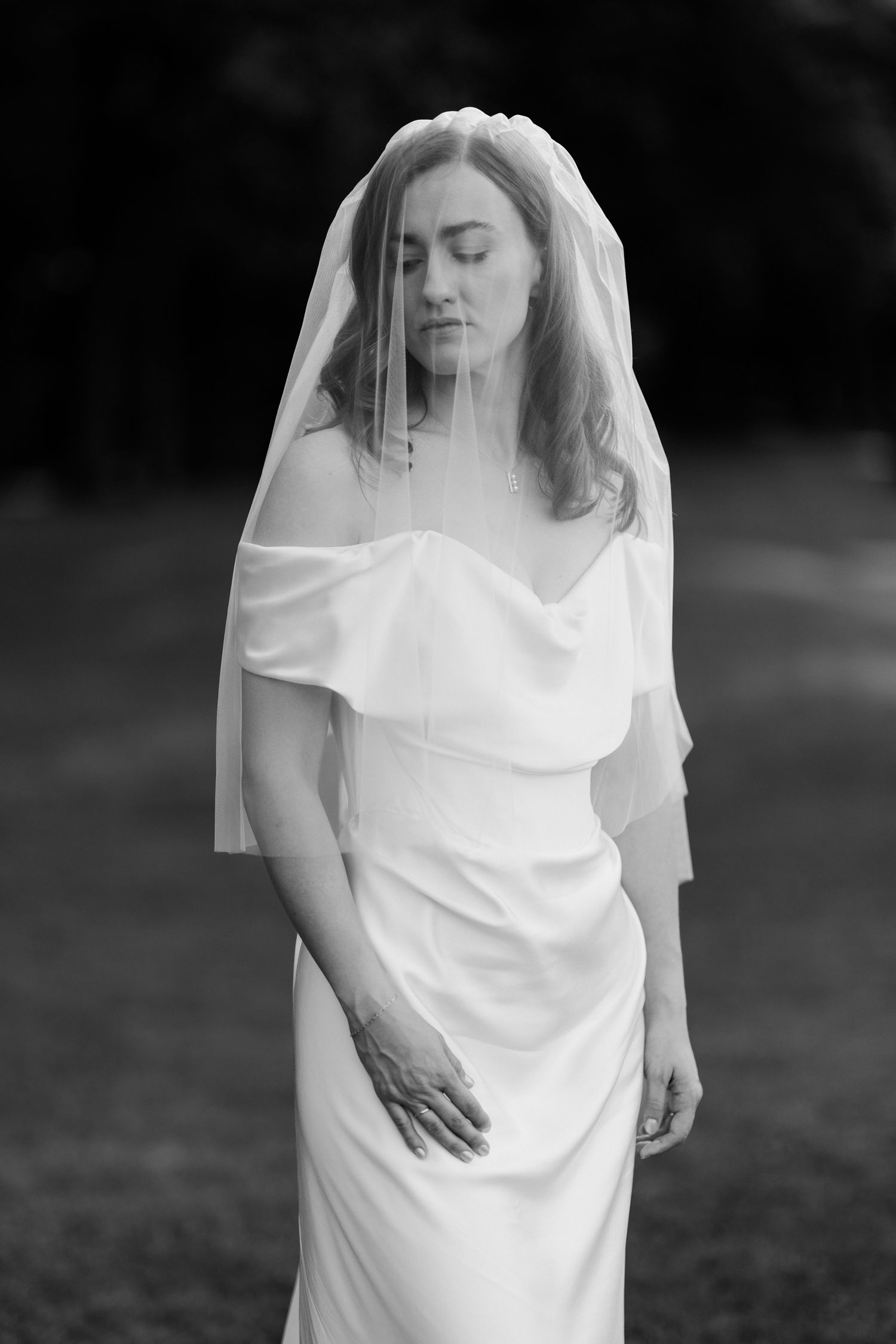 A person in a flowing white veil and dress stands in a dreamy outdoor setting in black and white. Editorial wedding photographer