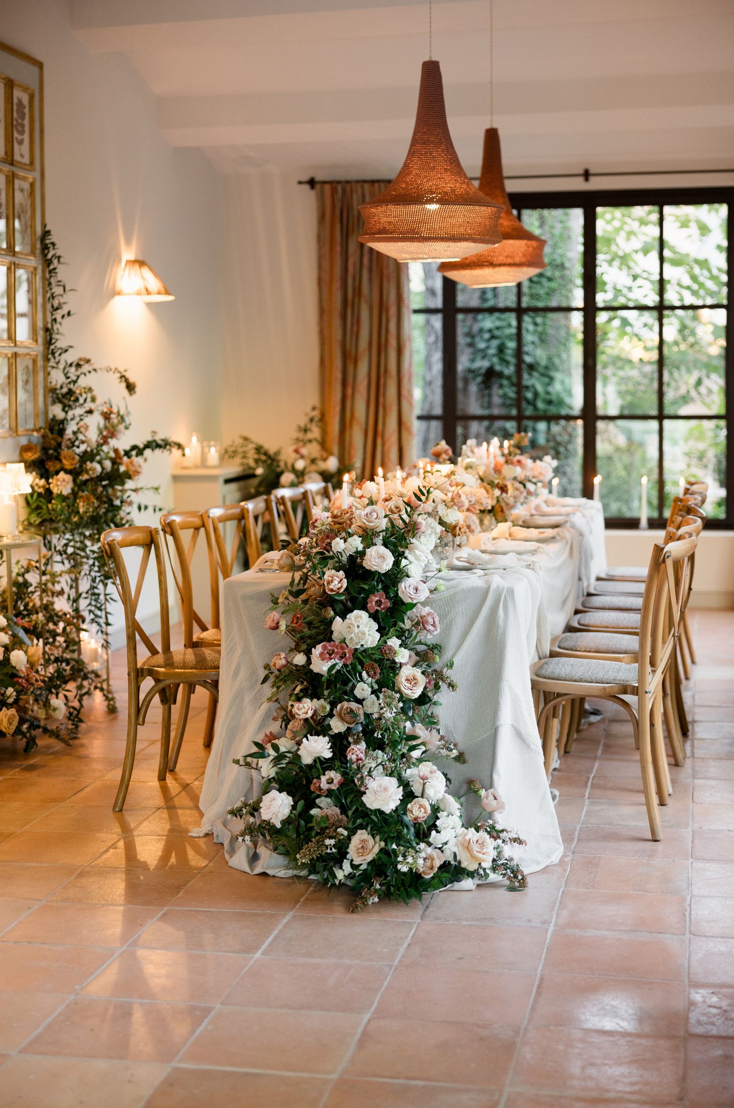 Elegant wedding reception tables decorated with white linens and floral arrangements in a bright, airy venue with terra cotta floors.