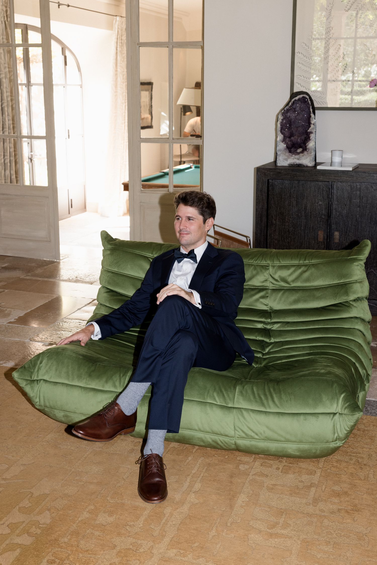 A sequence of photos showing a person in a suit reclining on a green velvet floor cushion in an empty room. Saint Remy de Provence