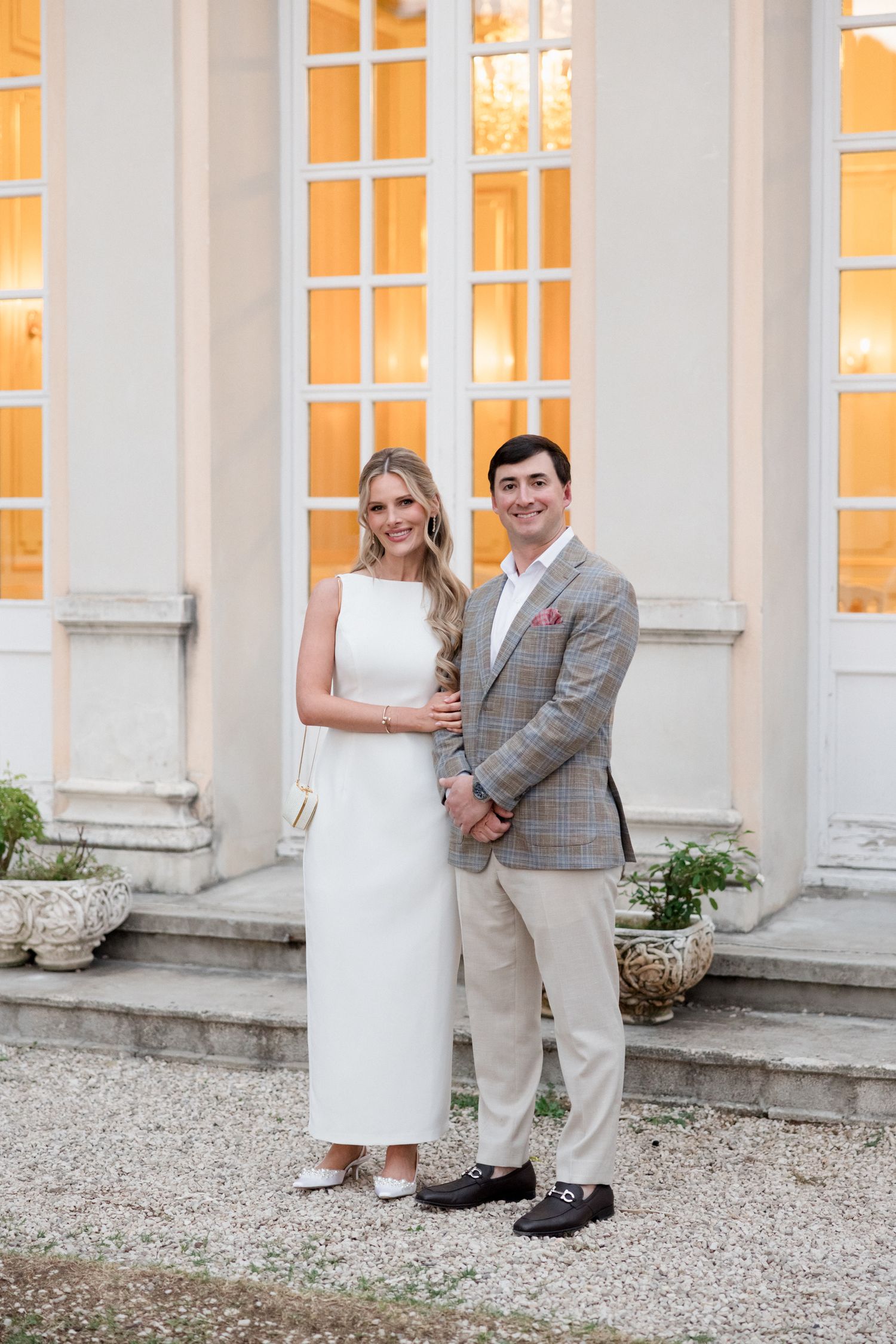 Wedding couple poses in elegant gray and white attire against a classic columned building exterior.