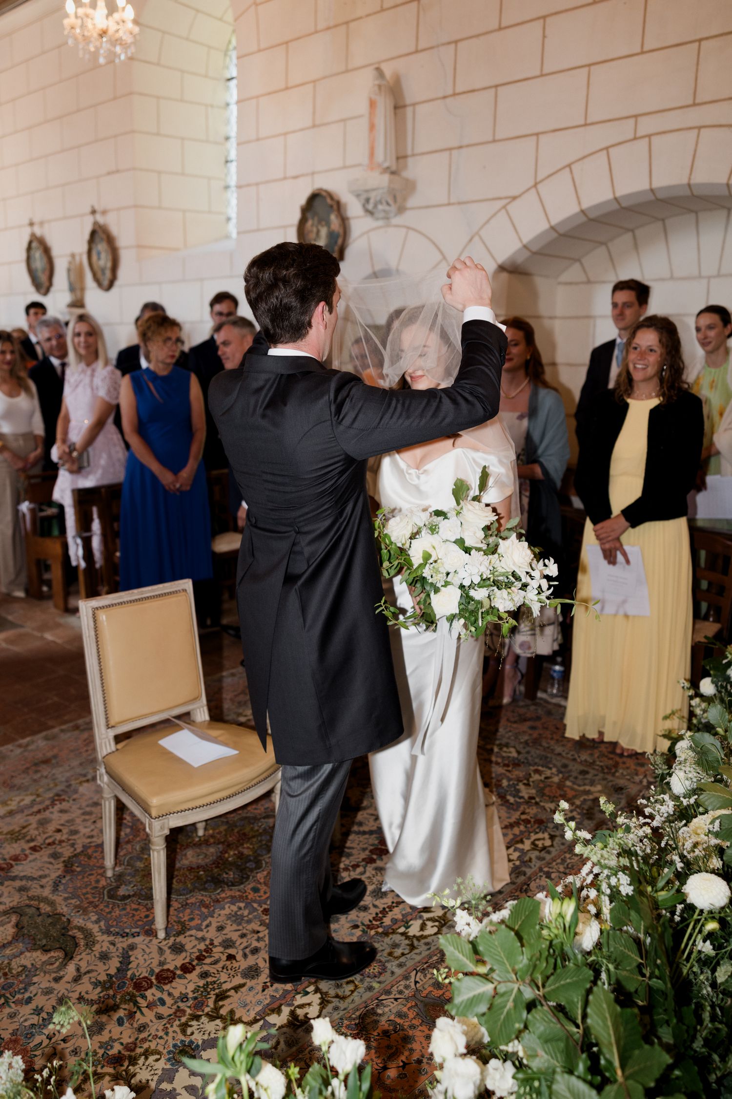 Wedding officiant gestures dramatically during ceremony in elegant stone-walled venue with floral decor.