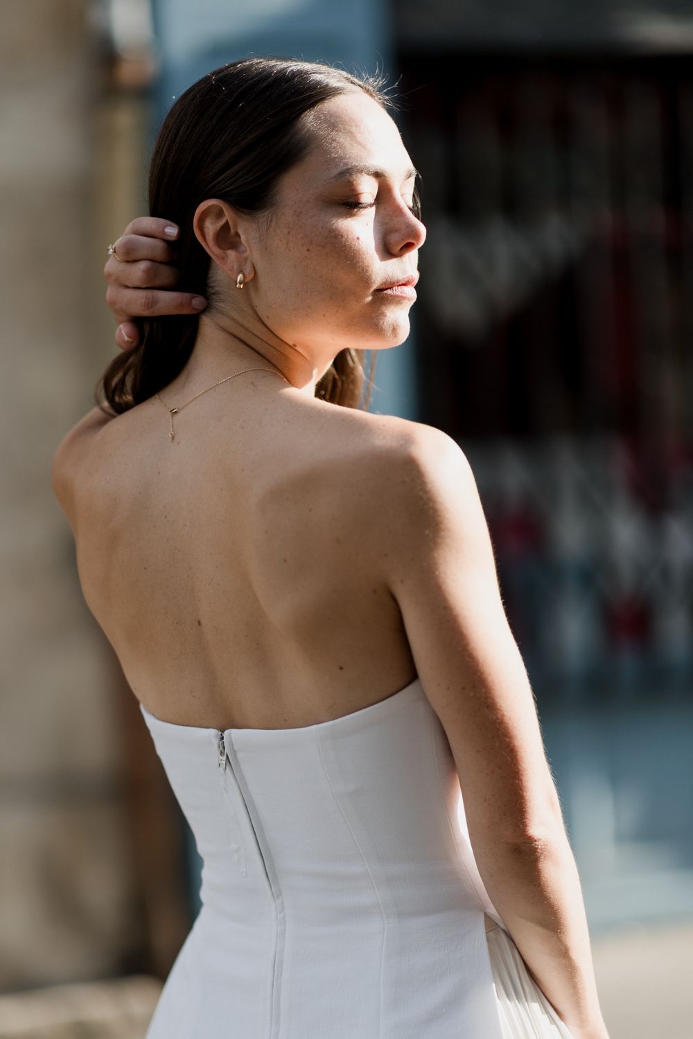 Person in white strapless dress standing in sunlight with eyes closed and hand touching hair. Seance couple Tours
