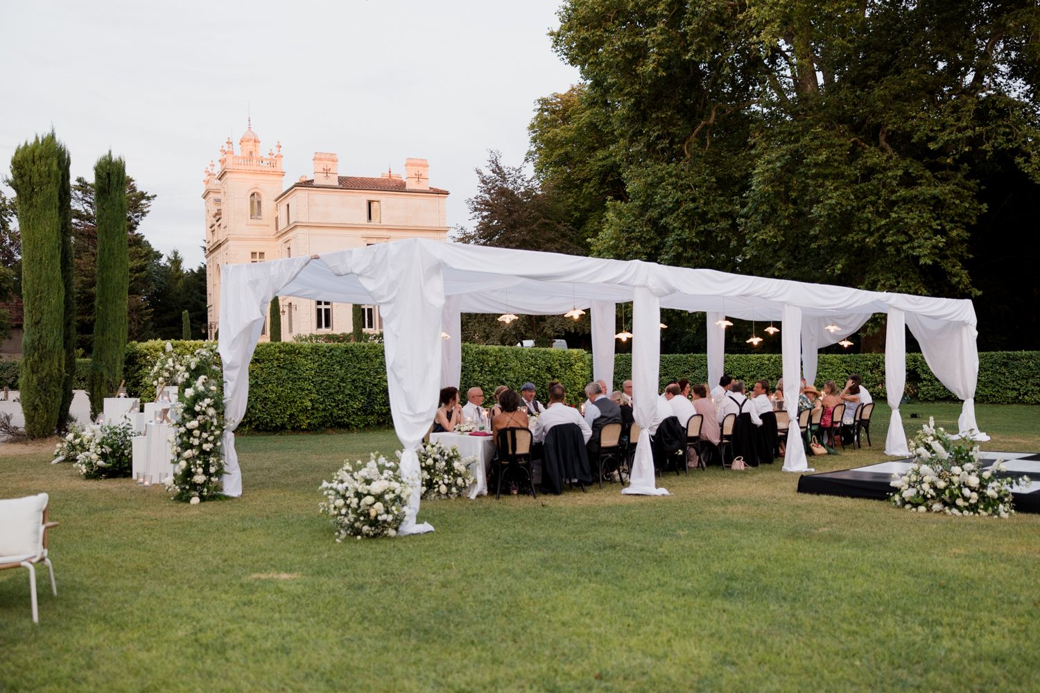 Elegant outdoor wedding ceremony setup with white drapes and chairs arranged on a lush green lawn. Château des 3 Fontaines