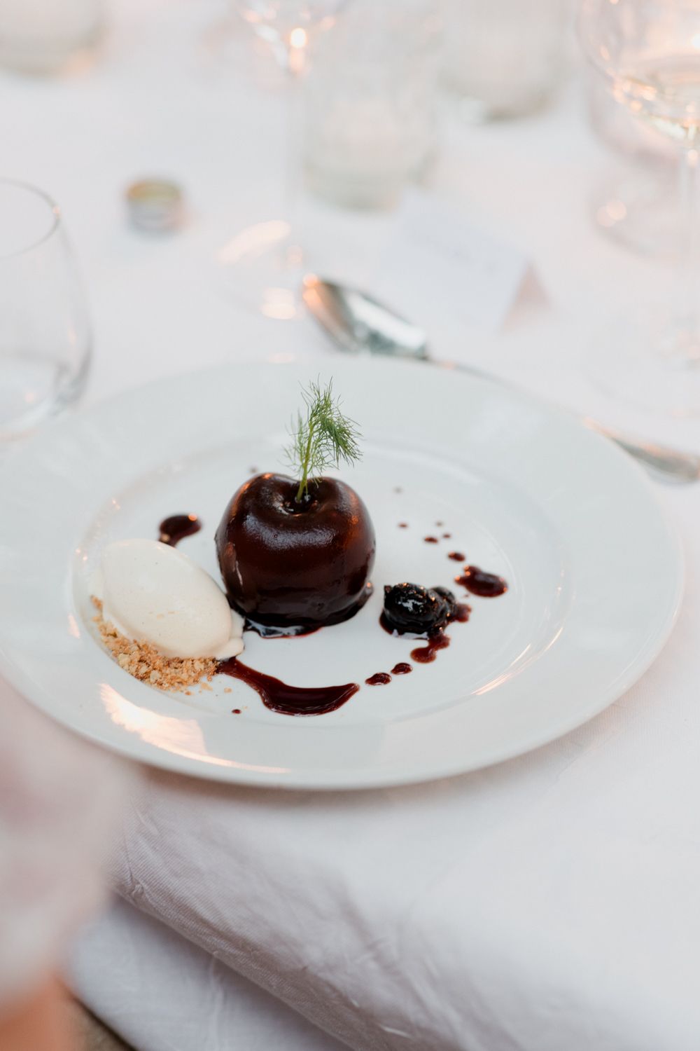 A dessert plate with dark chocolate-covered cherry garnished with fresh rosemary on a white plate. Welcome Event Auberge de la Treille
