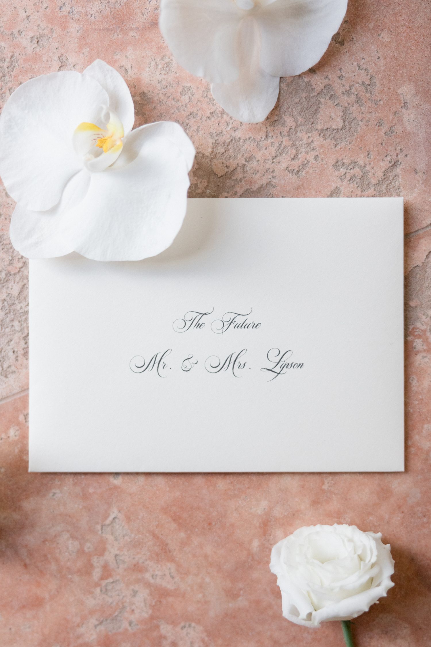 White orchid flowers and name cards arranged on a textured pink surface create an elegant wedding detail composition. destination wedding fr