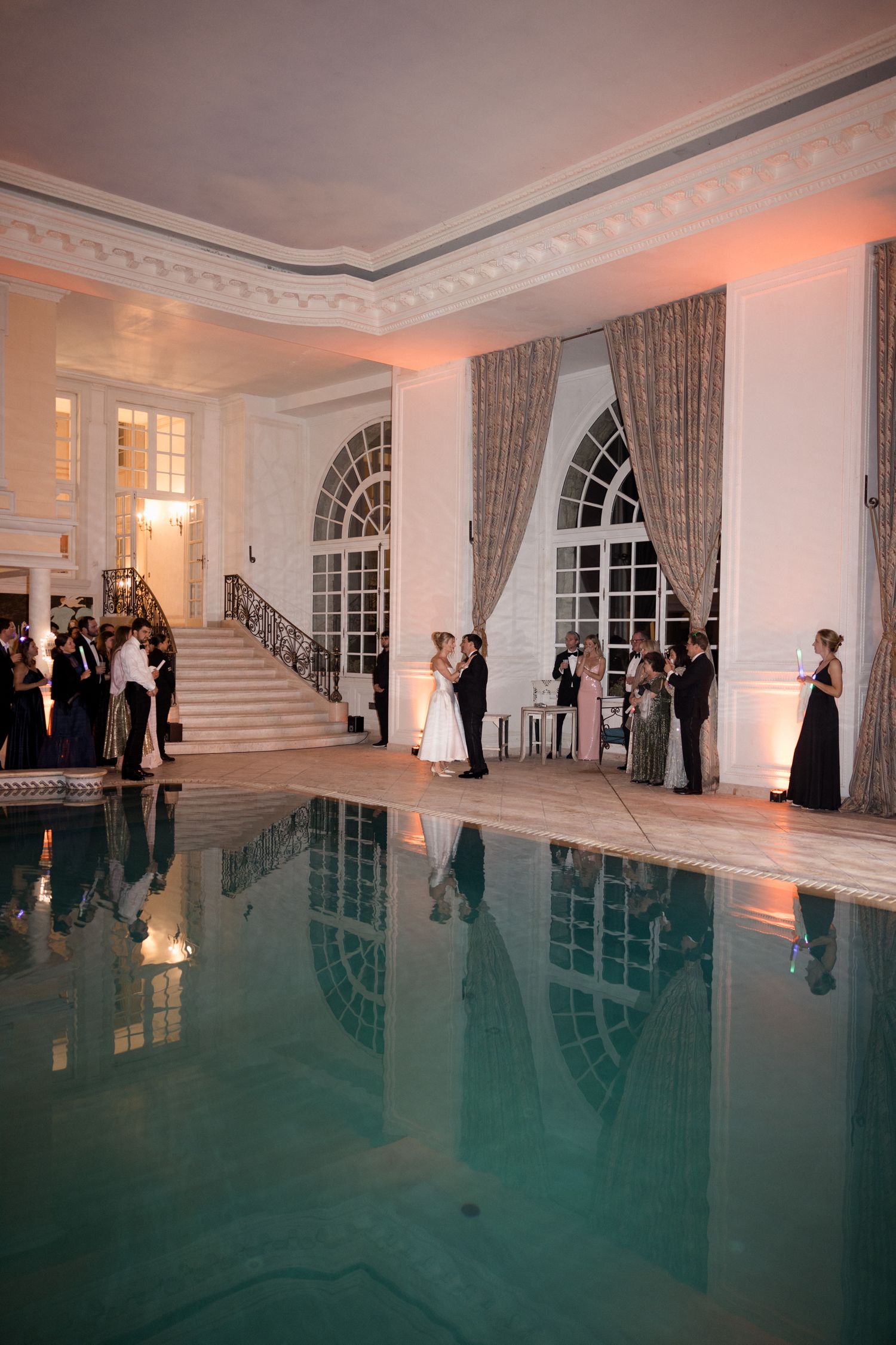 Elegant ballroom with white walls and turquoise reflective floor creates an illusion of water during an evening event.
