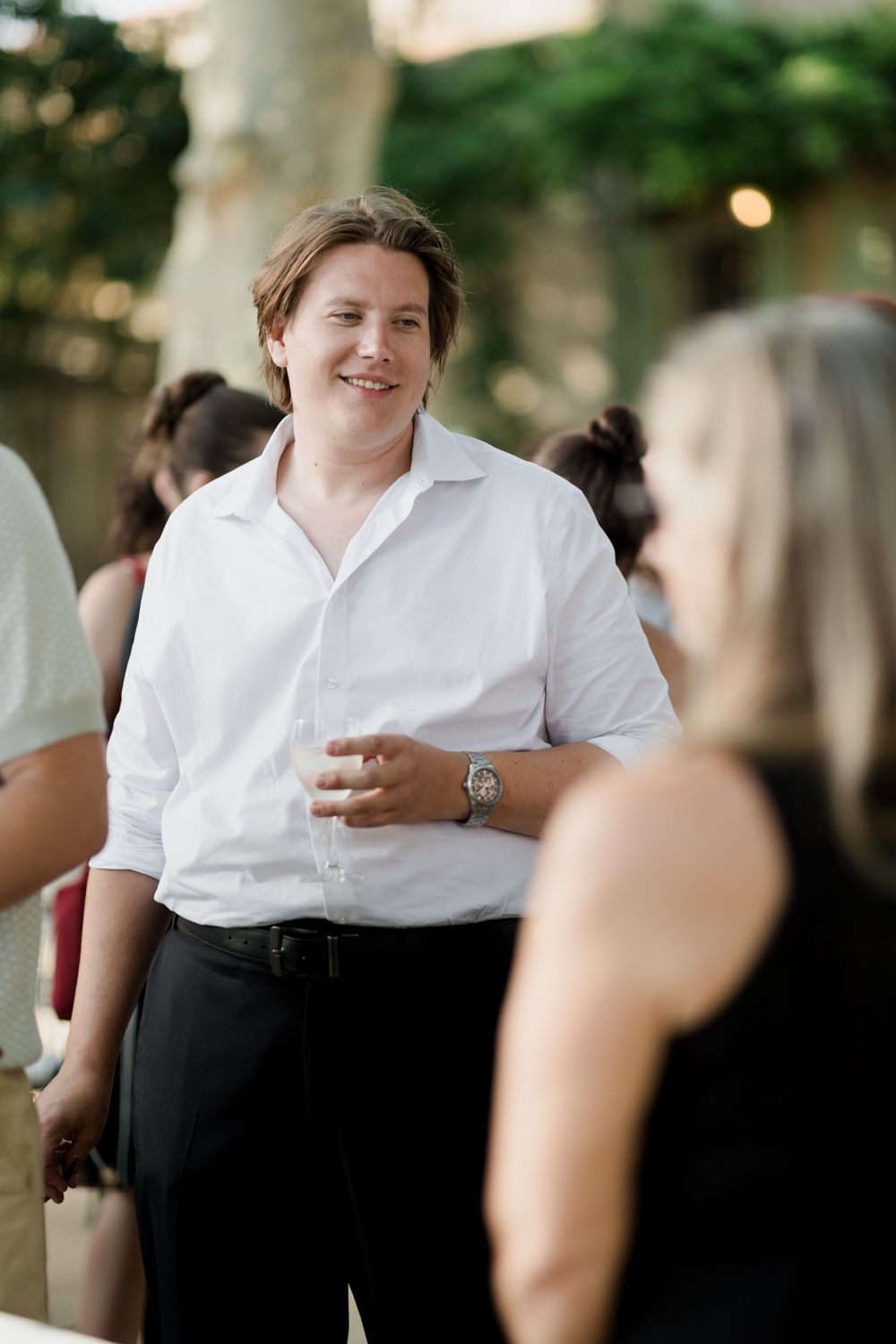Catering staff in white shirts and black pants serve guests at an outdoor event.