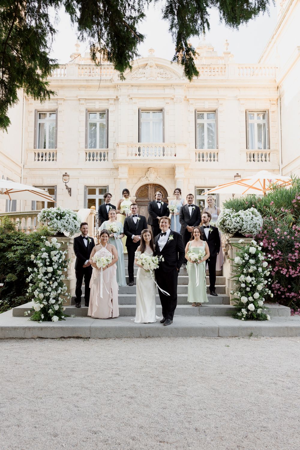 Elegant wedding party lined up outside a grand white building with beautiful floral arrangements.