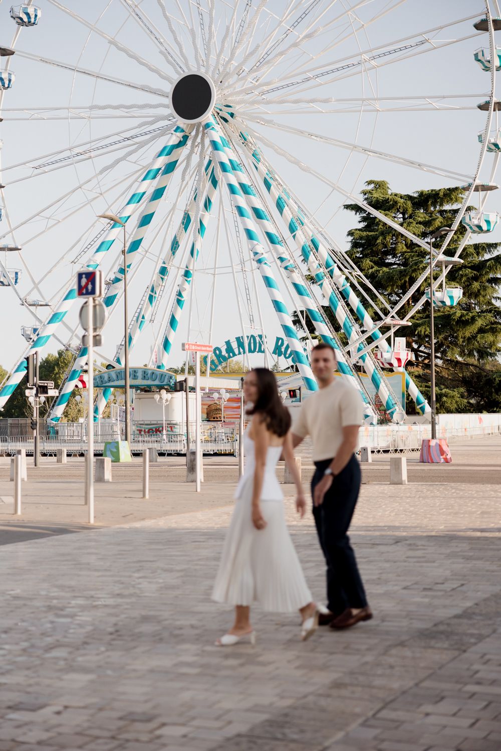 People dancing under a modern white and teal umbrella-like structure at an outdoor plaza area. Seance couple Tours
