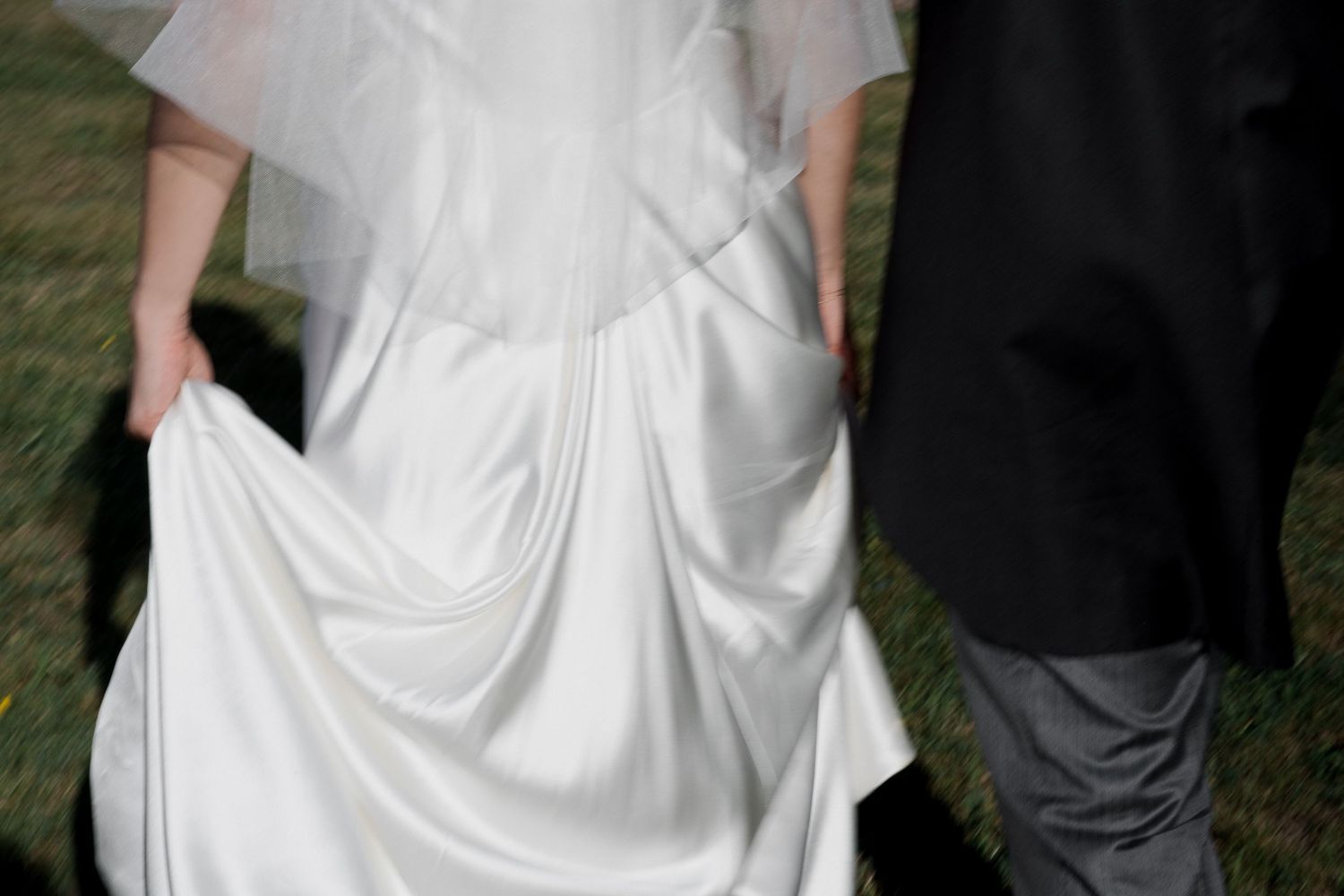 A bride in a white wedding dress poses with her bridesmaids wearing black dresses at an outdoor event.