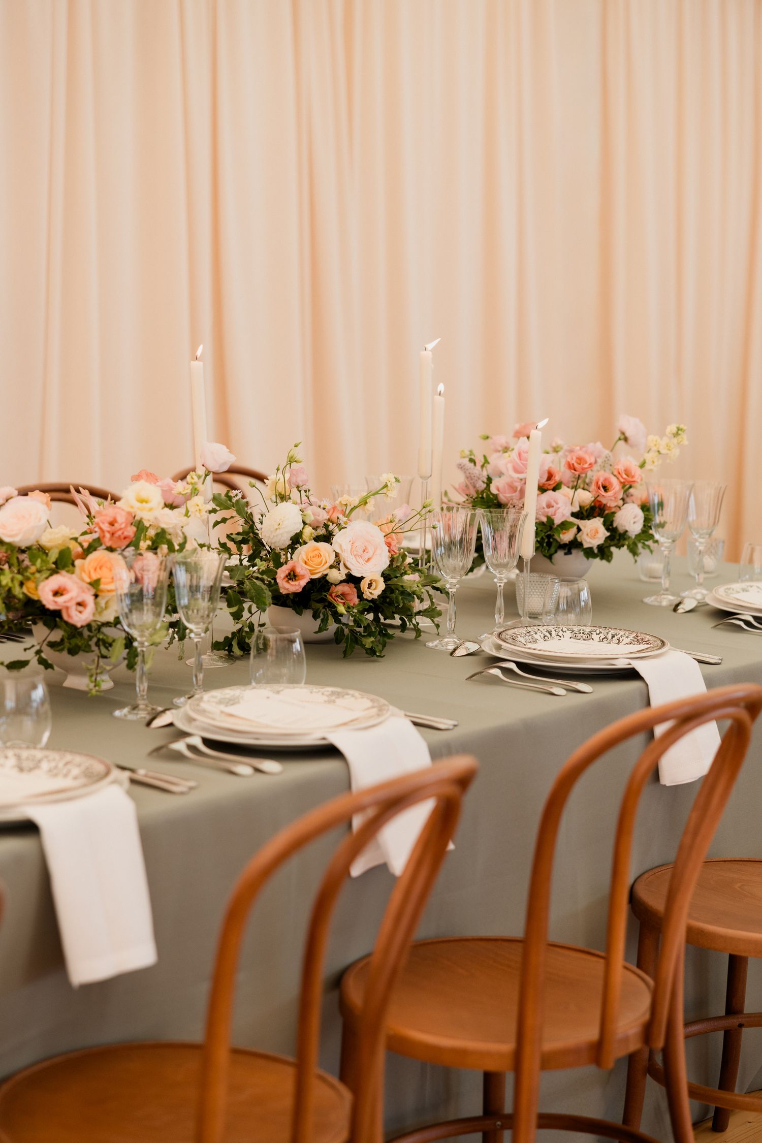 Elegant wedding reception table with pink floral centerpieces, wooden chairs and gray tablecloth.
