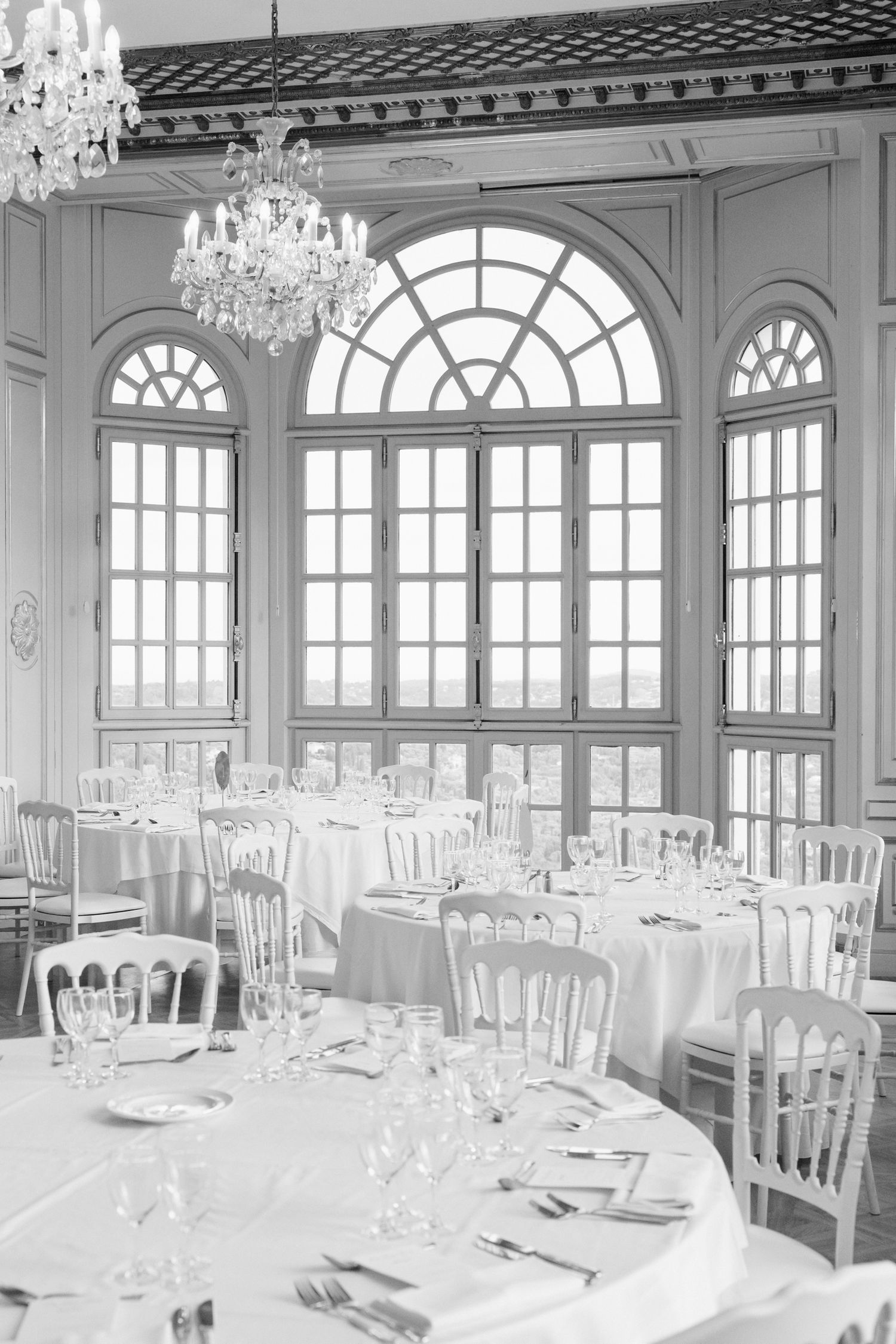 Elegant banquet hall with crystal chandeliers, arched windows, and white-clothed tables set for a formal dining event. mariage grasse